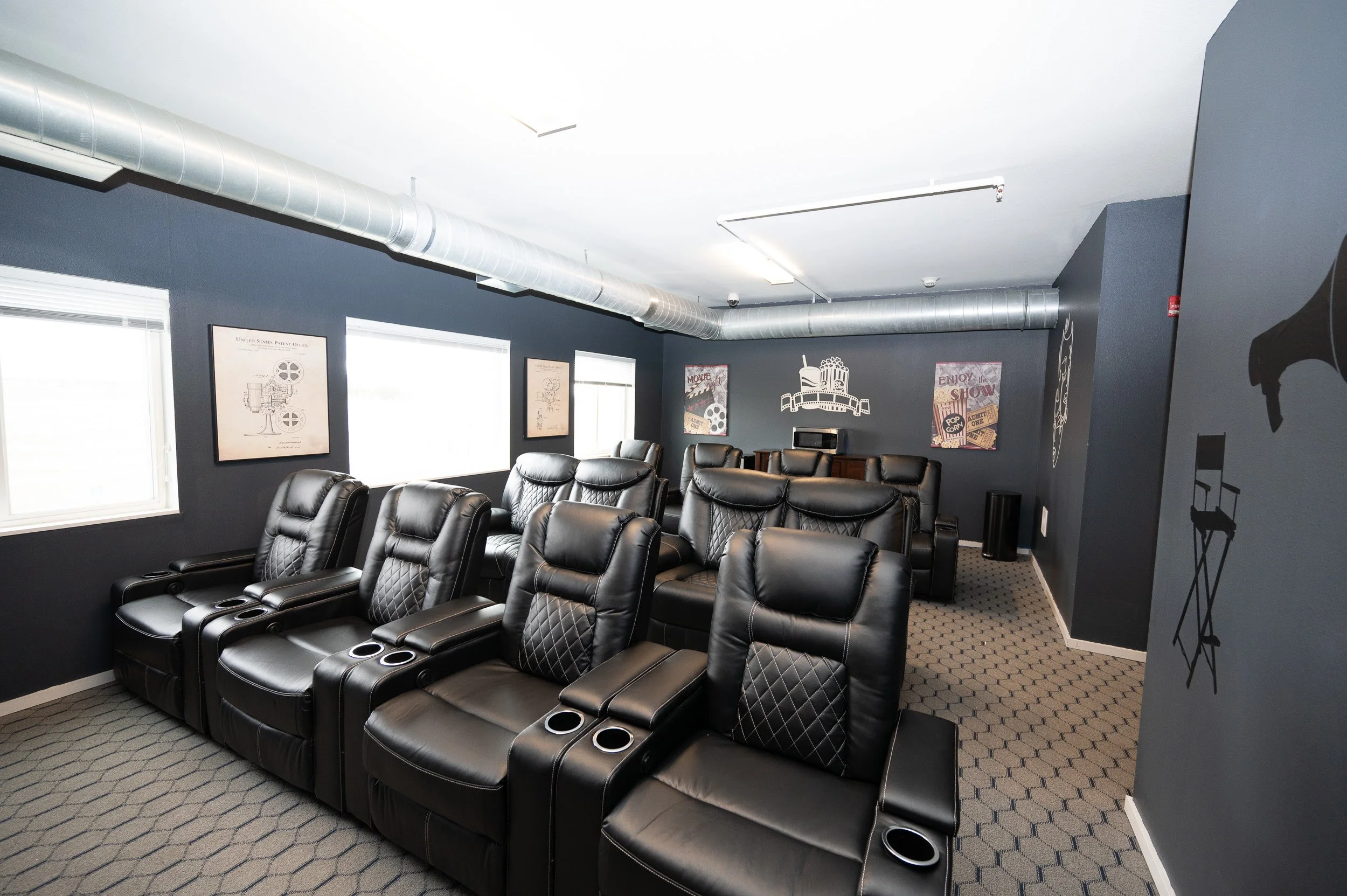 Home theater room in apartments in Rochester with black leather recliners, gray walls, movie art, and natural light from windows.