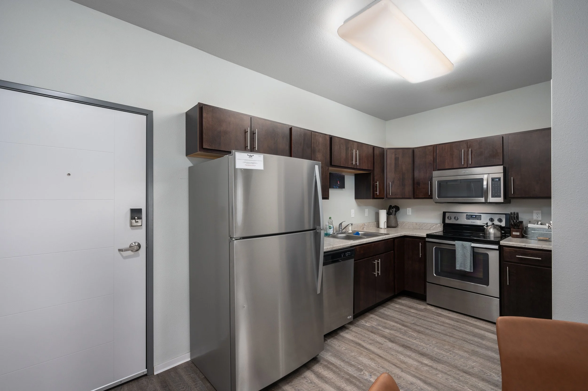 Modern kitchen in apartments in Rochester with stainless steel appliances, dark wood cabinets, and bright ceiling lighting.