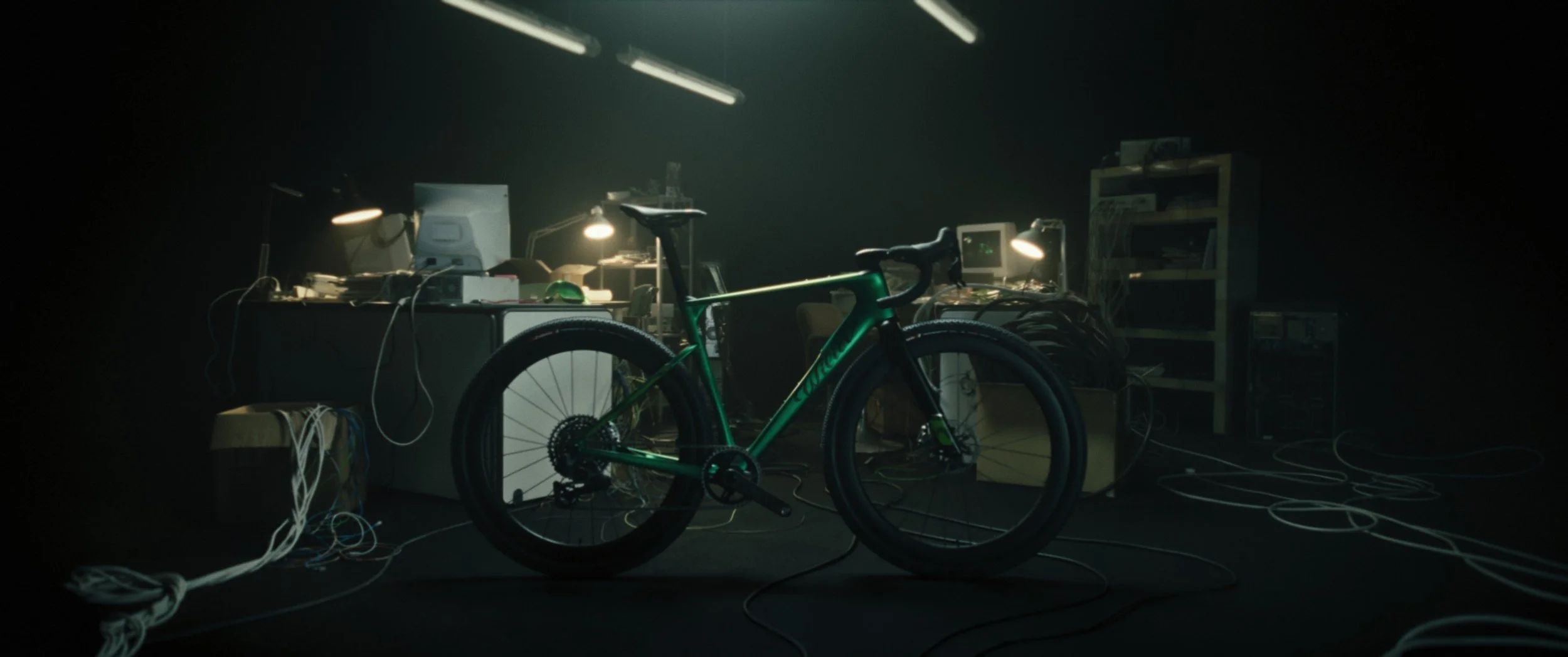 Una bicicletta da corsa verde in un ambiente oscuro, circondata da cavi e attrezzature da computer, con luci puntate sulla bicicletta.