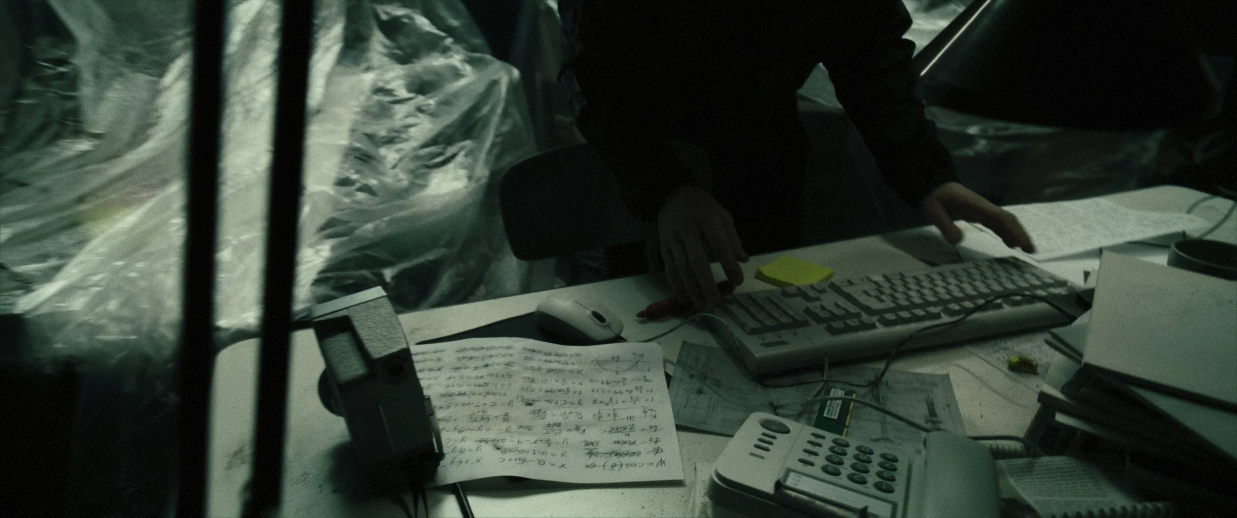 Uomo al lavoro in un ufficio con scrivania disordinata, toccando la tastiera del computer, circondato da carta, telefoni e altri dispositivi elettronici.