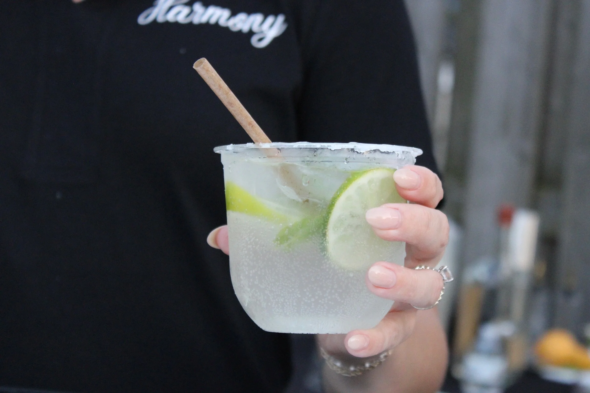 Person holding a clear cup with a lemon and lime infused sparkling water and a cinnamon stick, with visible condensation on the outside of the cup.