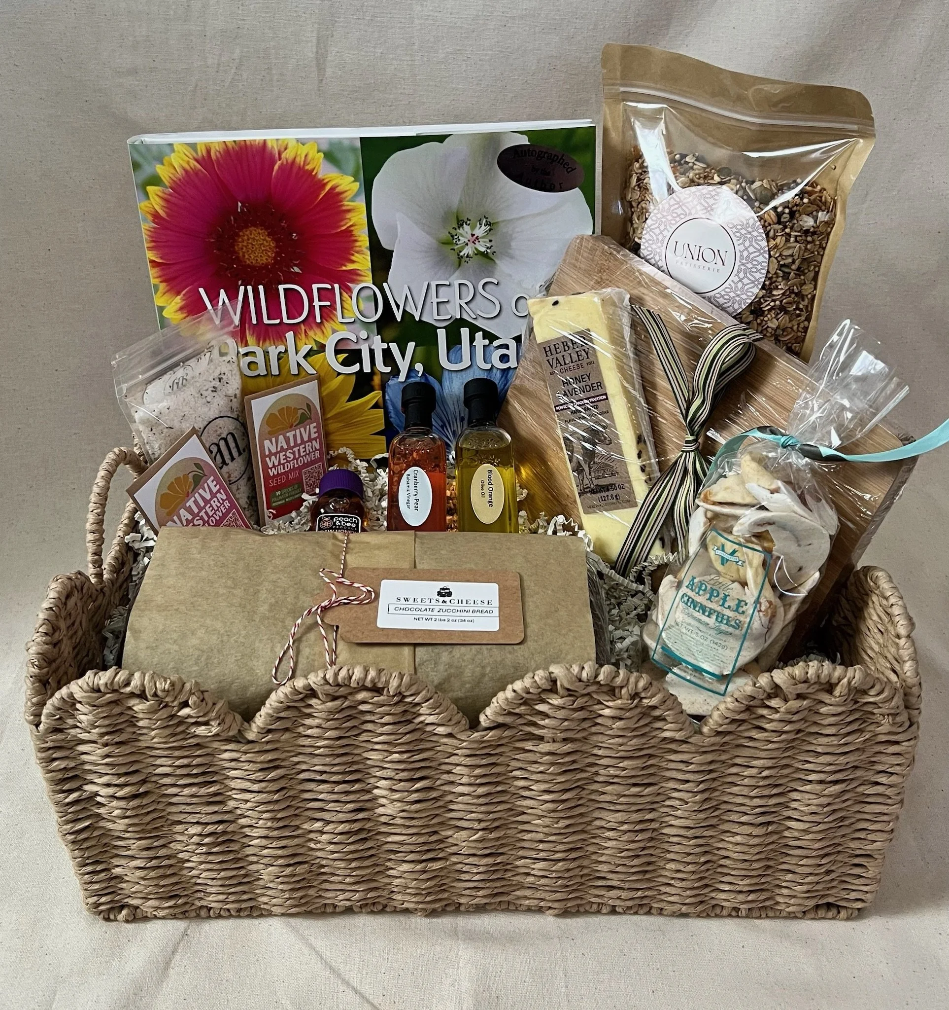 A woven basket filled with various food products and items, including snacks, beverages, and packaged goods, arranged on a countertop.
