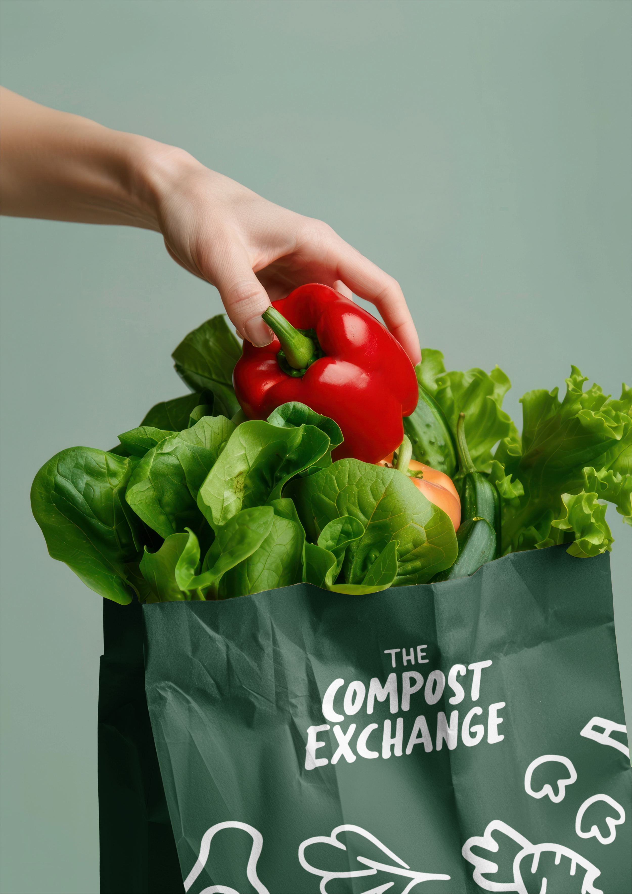 A hand placing a red bell pepper into a bag filled with green leafy vegetables, with the bag labeled "The Compost Exchange."