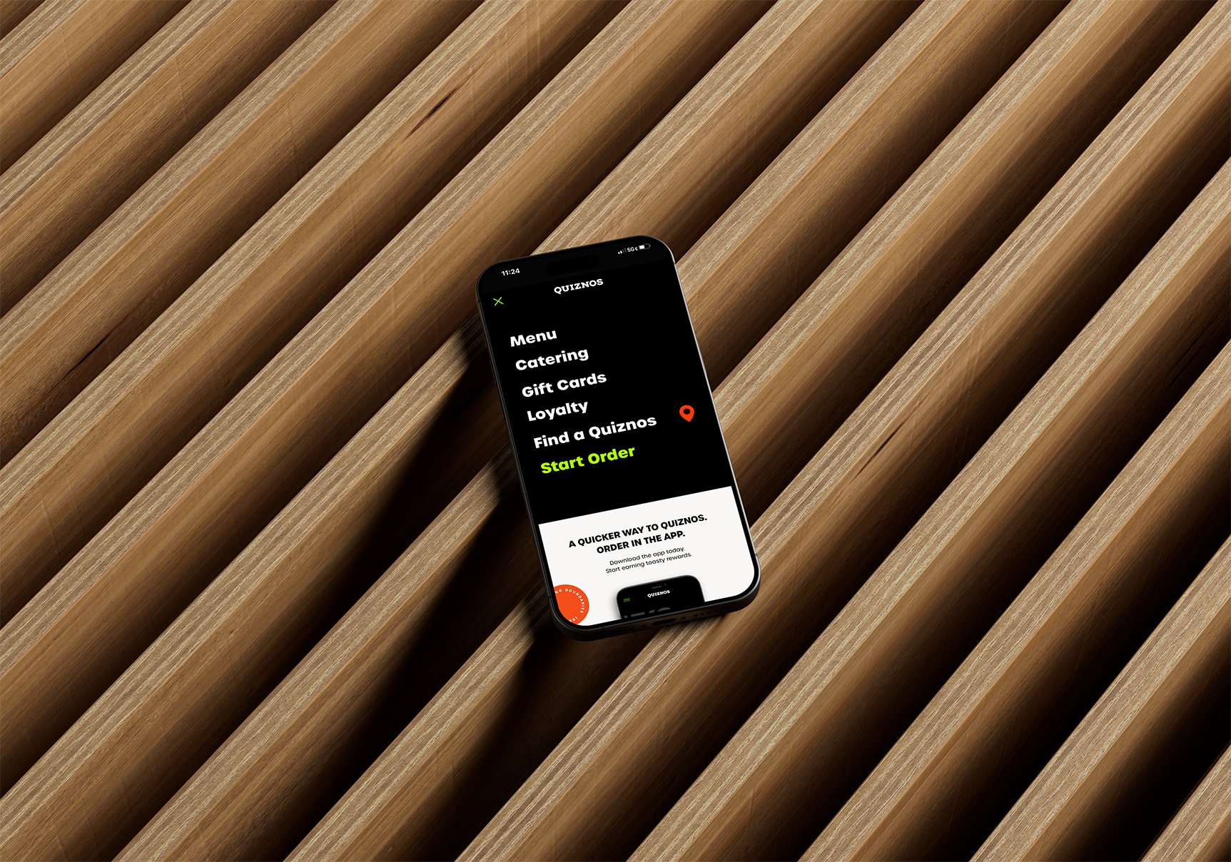 A smartphone displaying the Quiznos app menu on a wooden surface with diagonal slats.