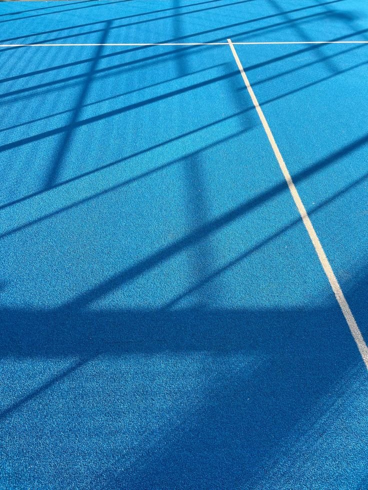 Shadows of a fence cast on a blue sports court with white lines