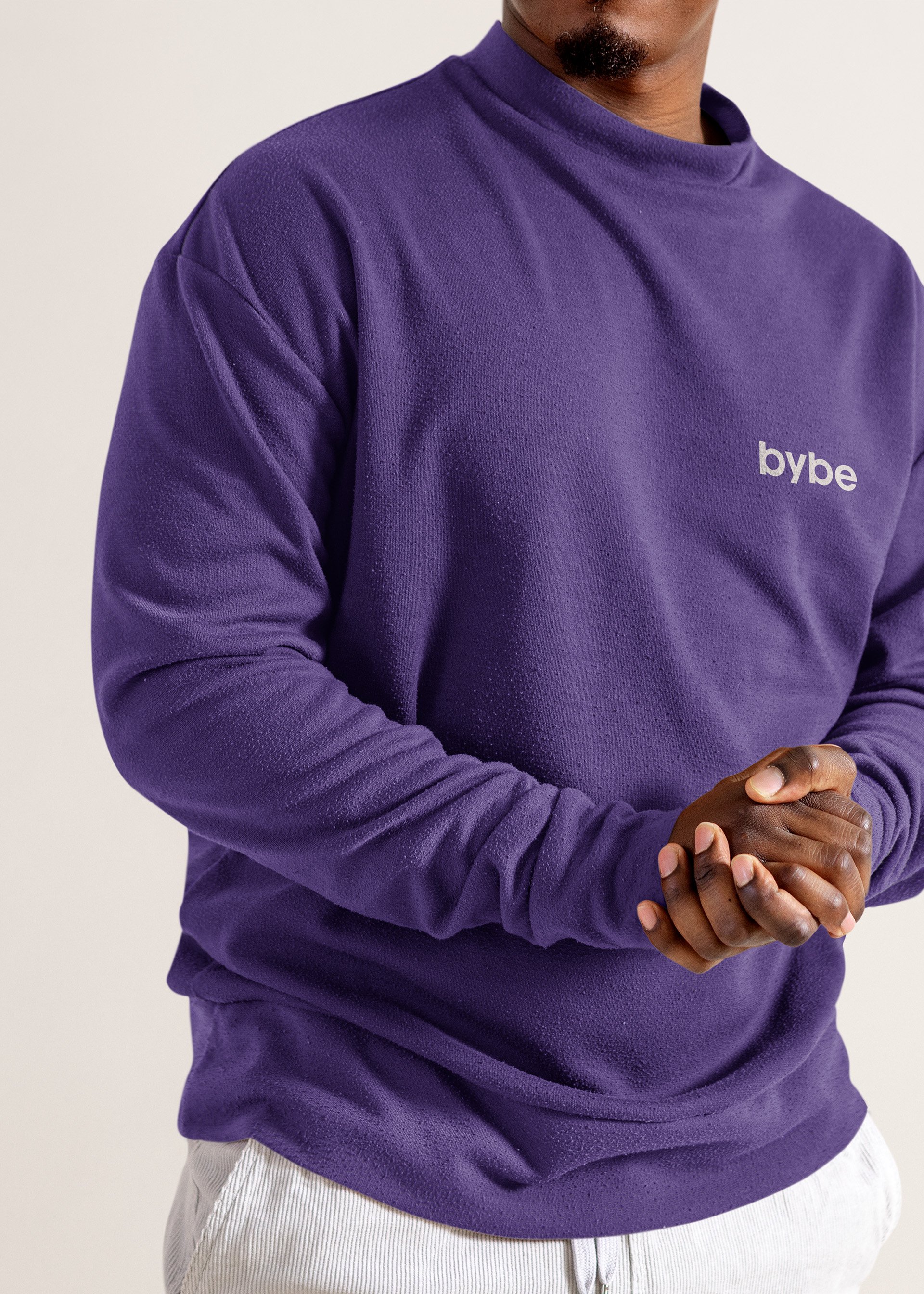 Close-up of a person wearing a purple sweatshirt with the word 'bybe' printed on it, and clasping their hands together.