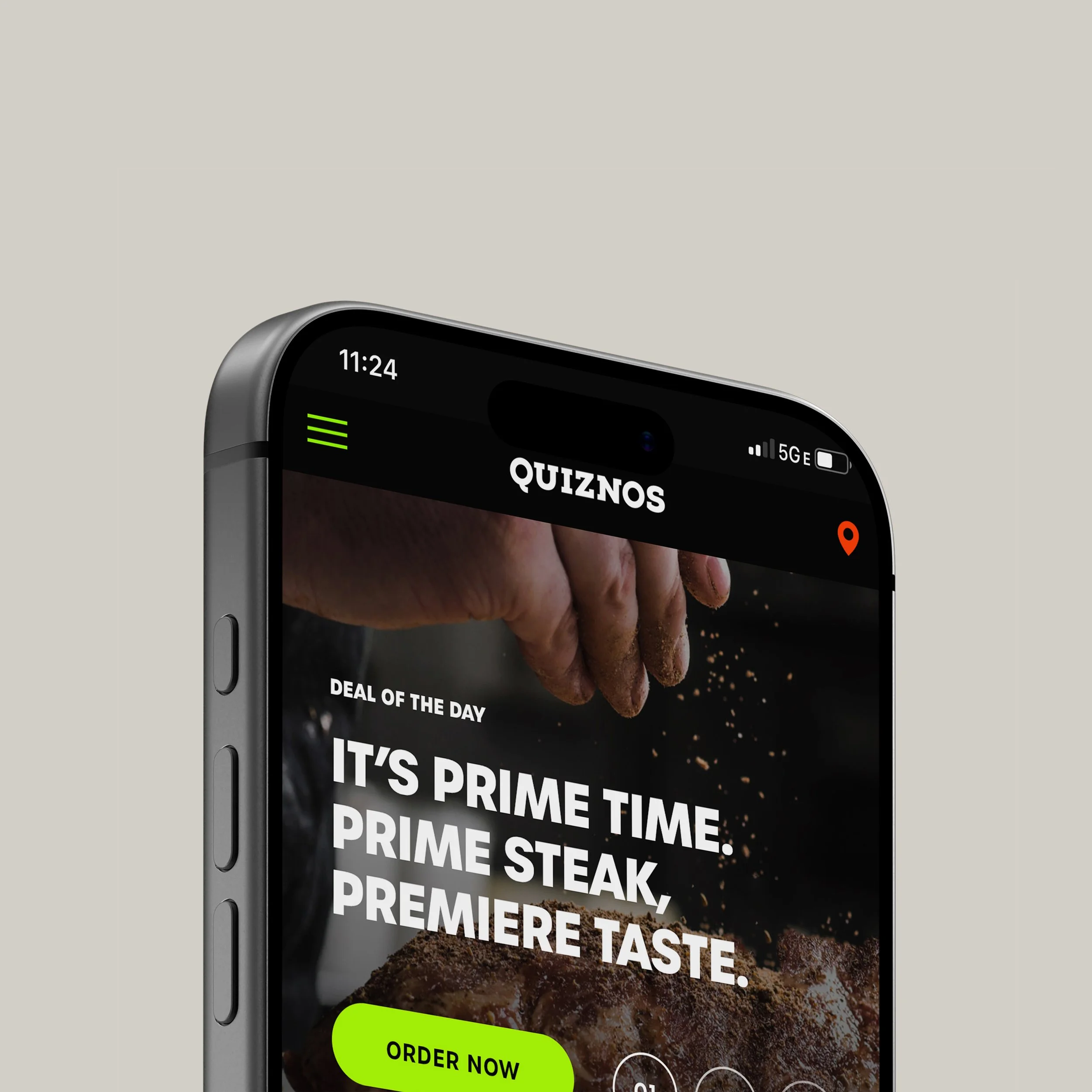 Close-up of a smartphone displaying the Quiznos app with a promotional ad for Prime steak, showing a hand sprinkling seasoning on a steak, and a neon green 'Order Now' button.