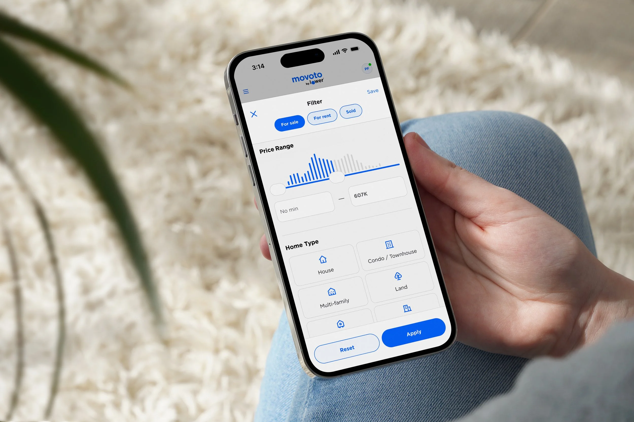 A person holding a smartphone displaying a real estate app filter screen with options to filter properties by price range, home type, and sale status.