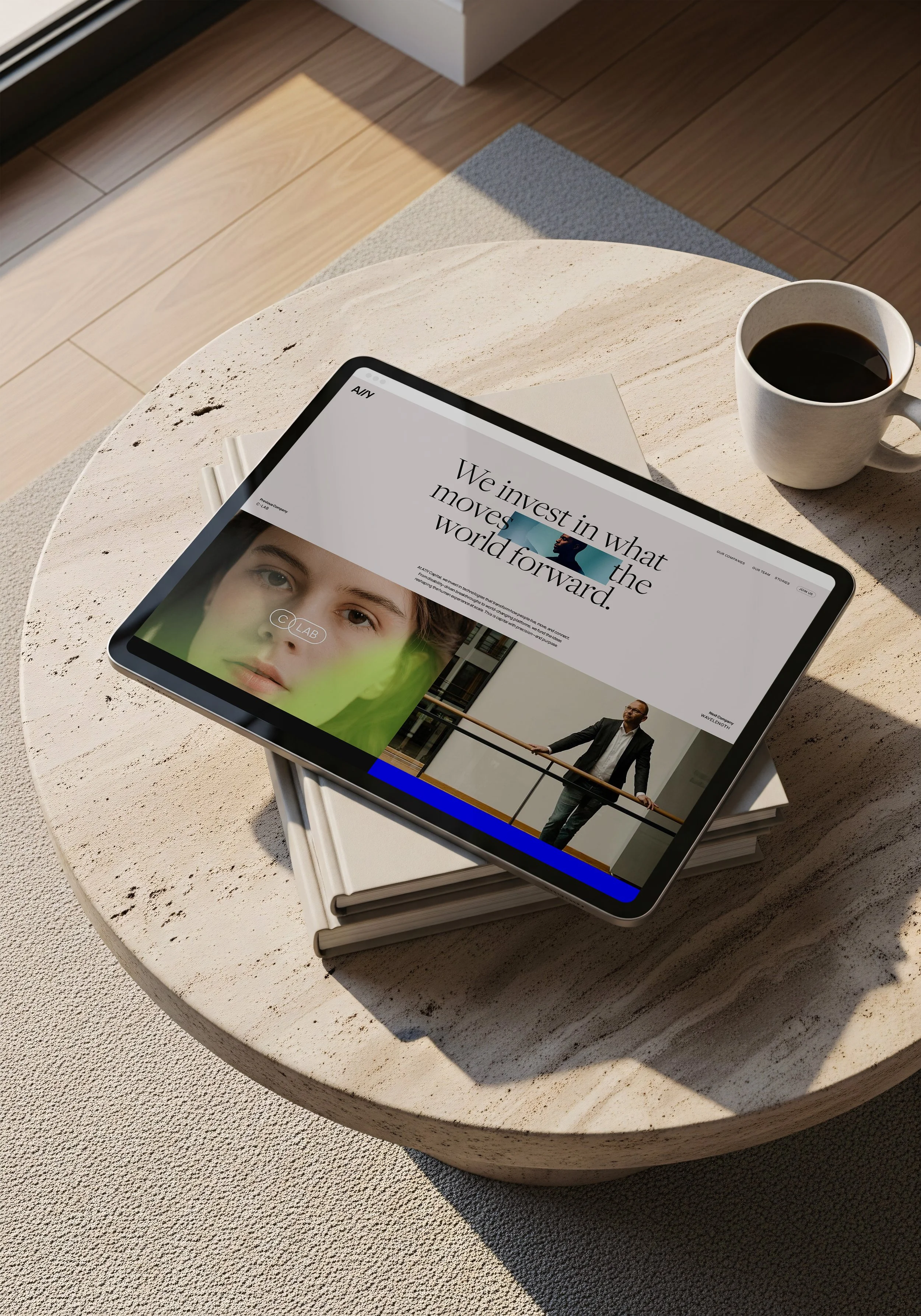 A tablet displaying a website, placed on a stack of books on a round table with a cup of coffee, in a well-lit room.
