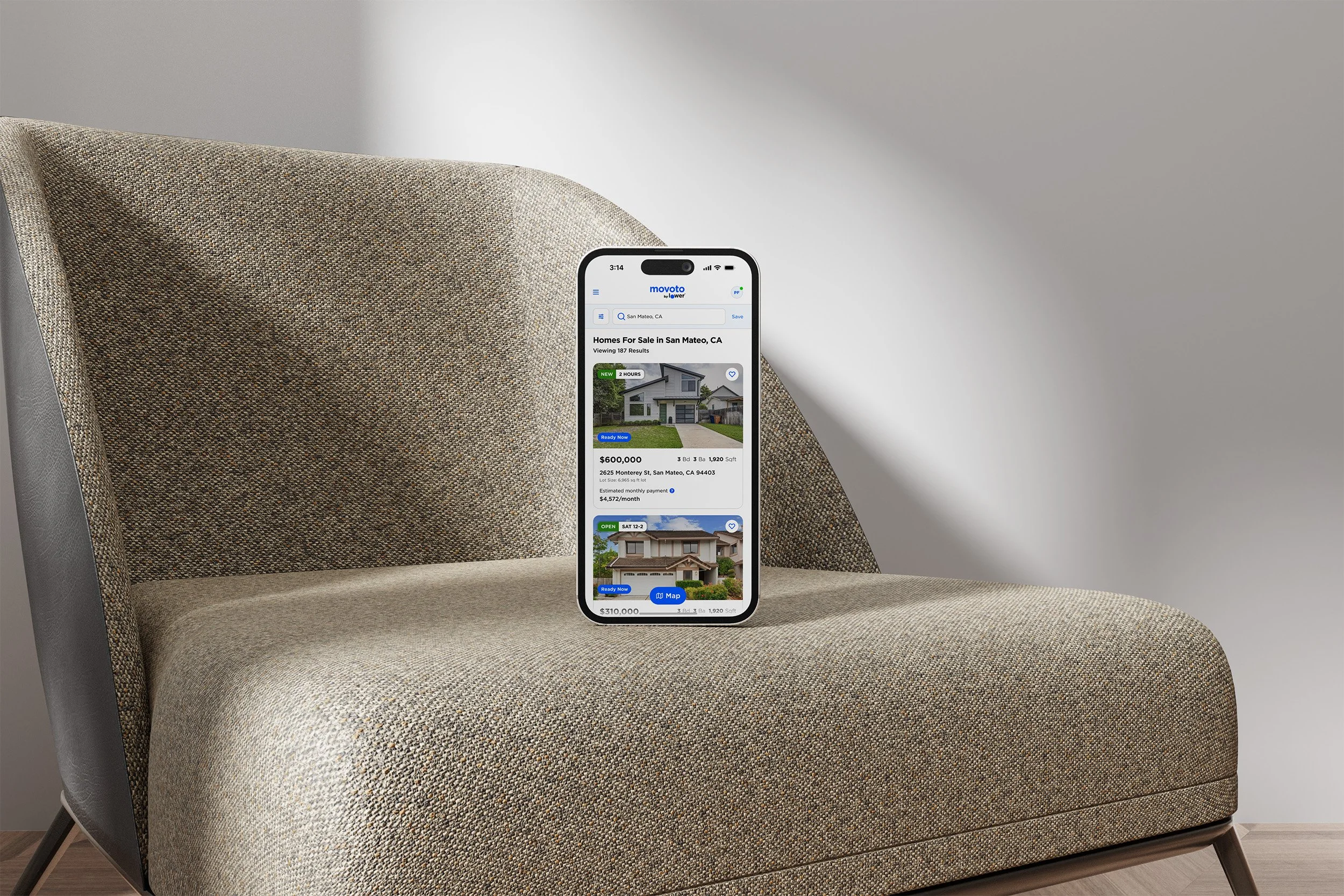 Smartphone displaying real estate listings on a beige fabric armchair.