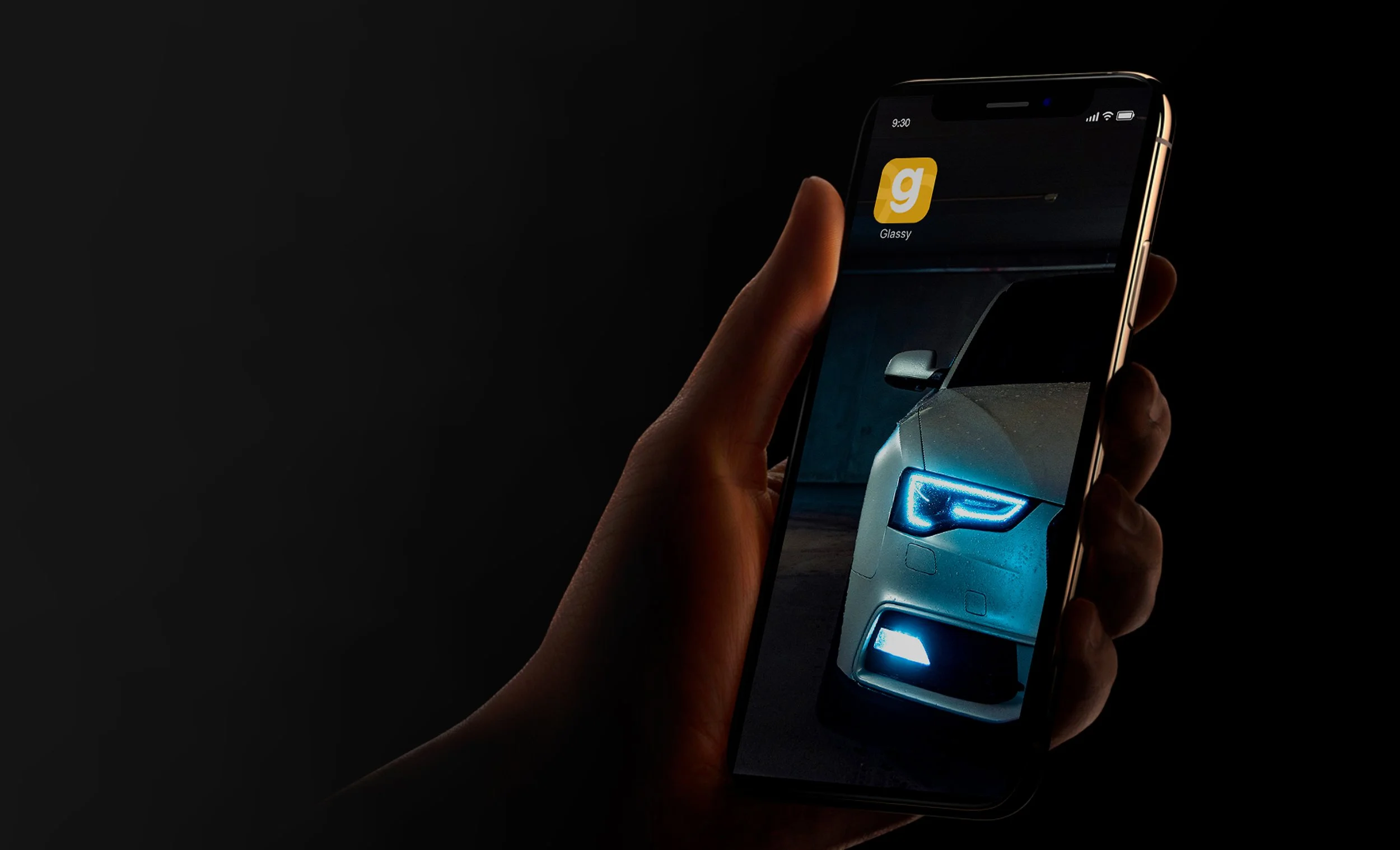 Close-up of a hand holding a smartphone displaying the front of a white car with blue headlights in a dark environment.