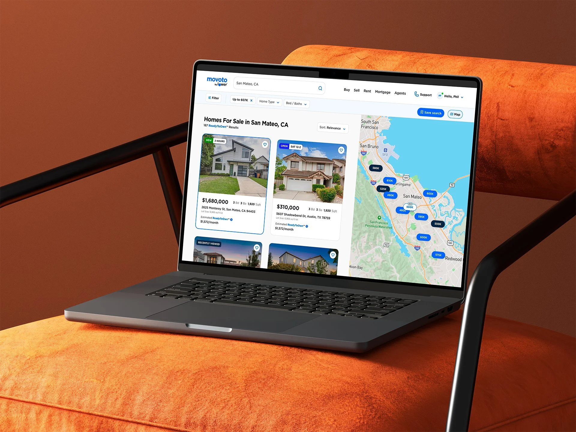 Open laptop displaying a real estate website with homes for sale in San Mateo, California, shown alongside a map with house prices marked on it, placed on an orange couch with a brown background.