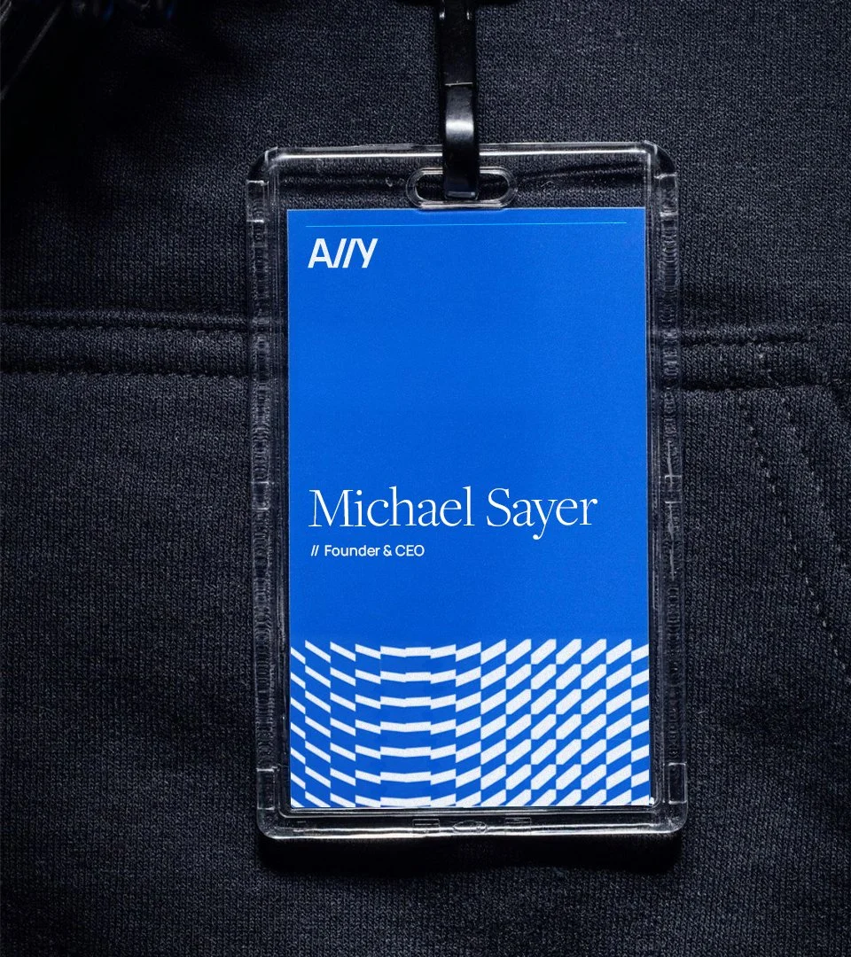 A conference badge with the name Michael Sayer, identified as Founder & CEO, attached to a person wearing a black textured fabric garment.