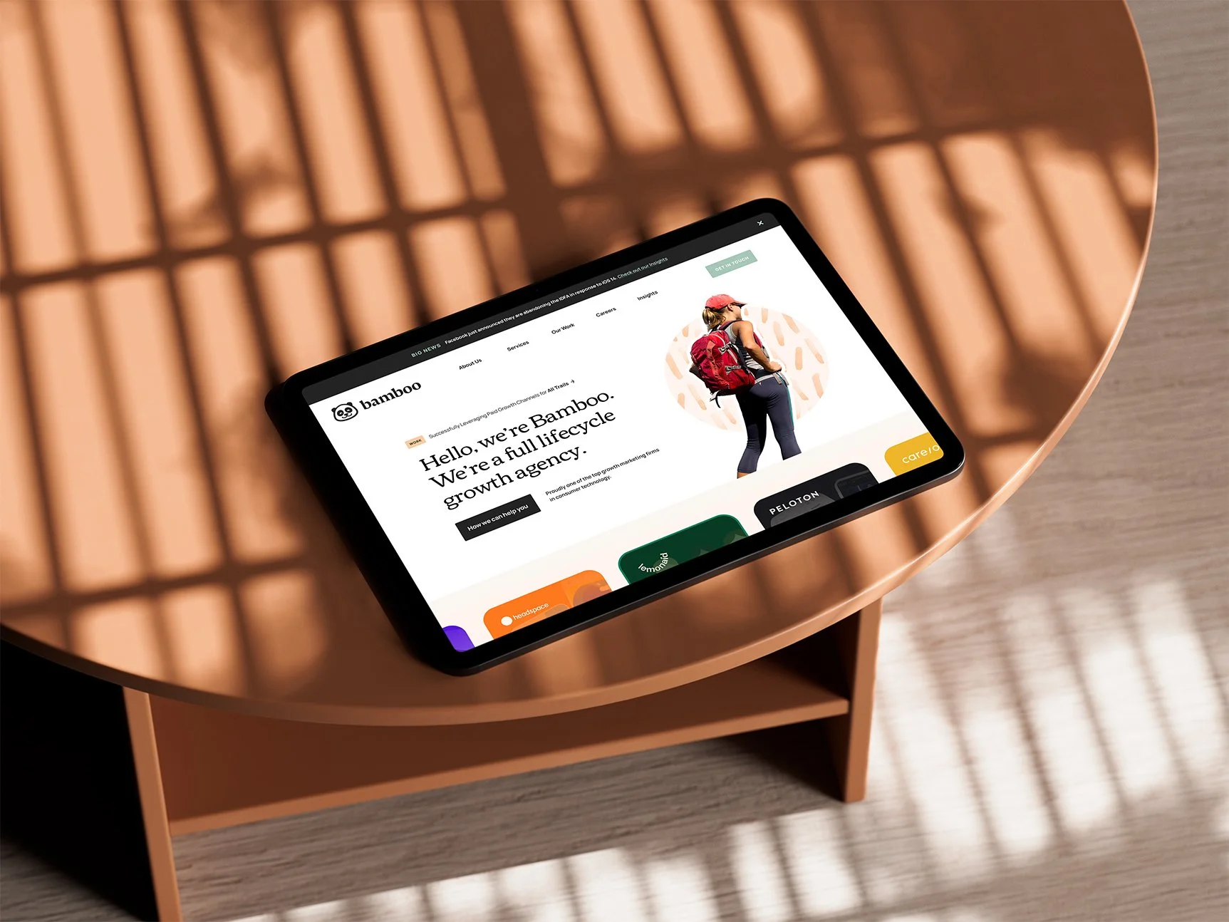 A tablet on a wooden table displaying a website for Bamboo, a full lifecycle growth agency, with a woman wearing a red cap and backpack on the screen.