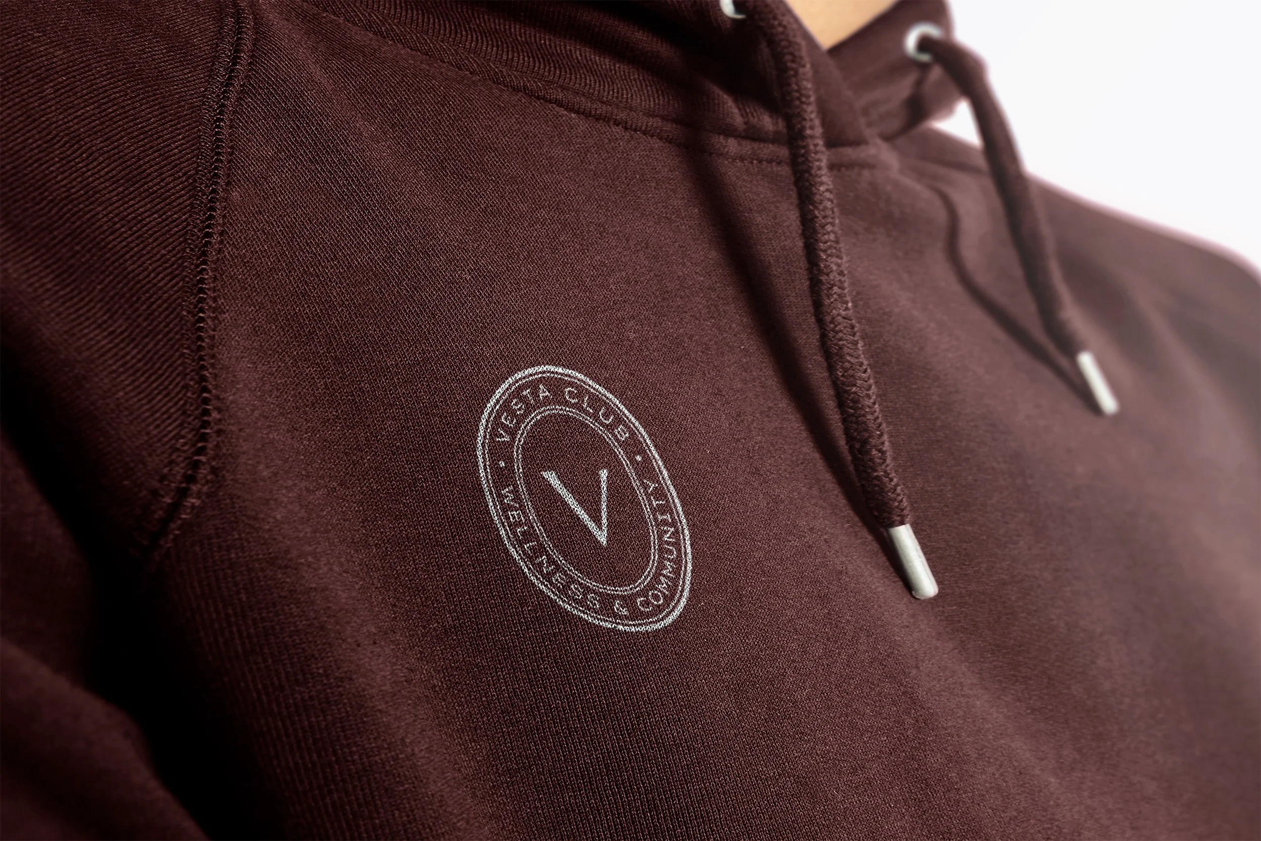 Close-up of a maroon hoodie with a circular logo on the chest that reads "Victoria Club, Virginia, Co. 1985" and features a large letter "V" in the center.