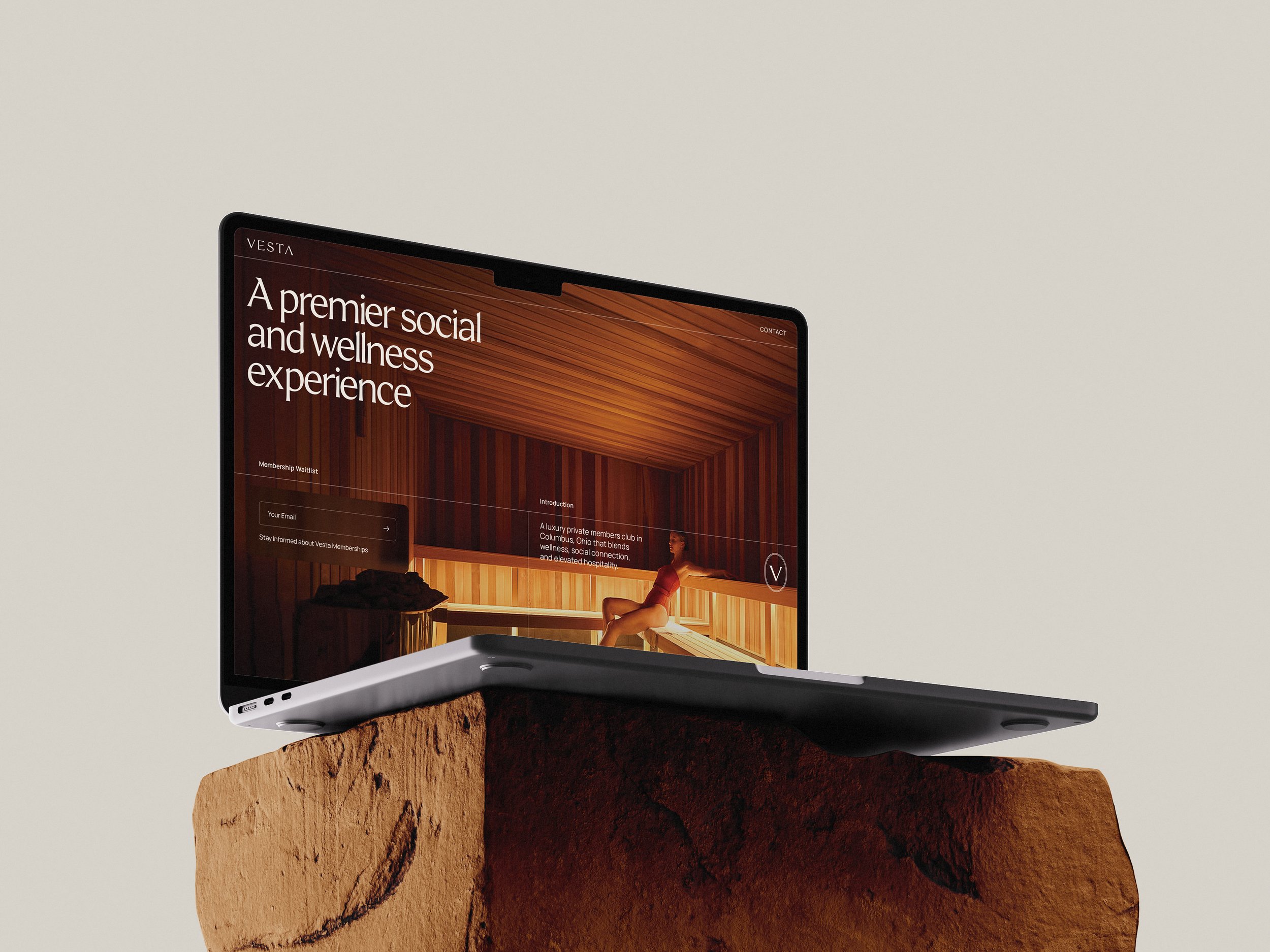 Laptop computer displaying a wellness and social experience website, placed on a rough brown rock against a plain light-colored background.