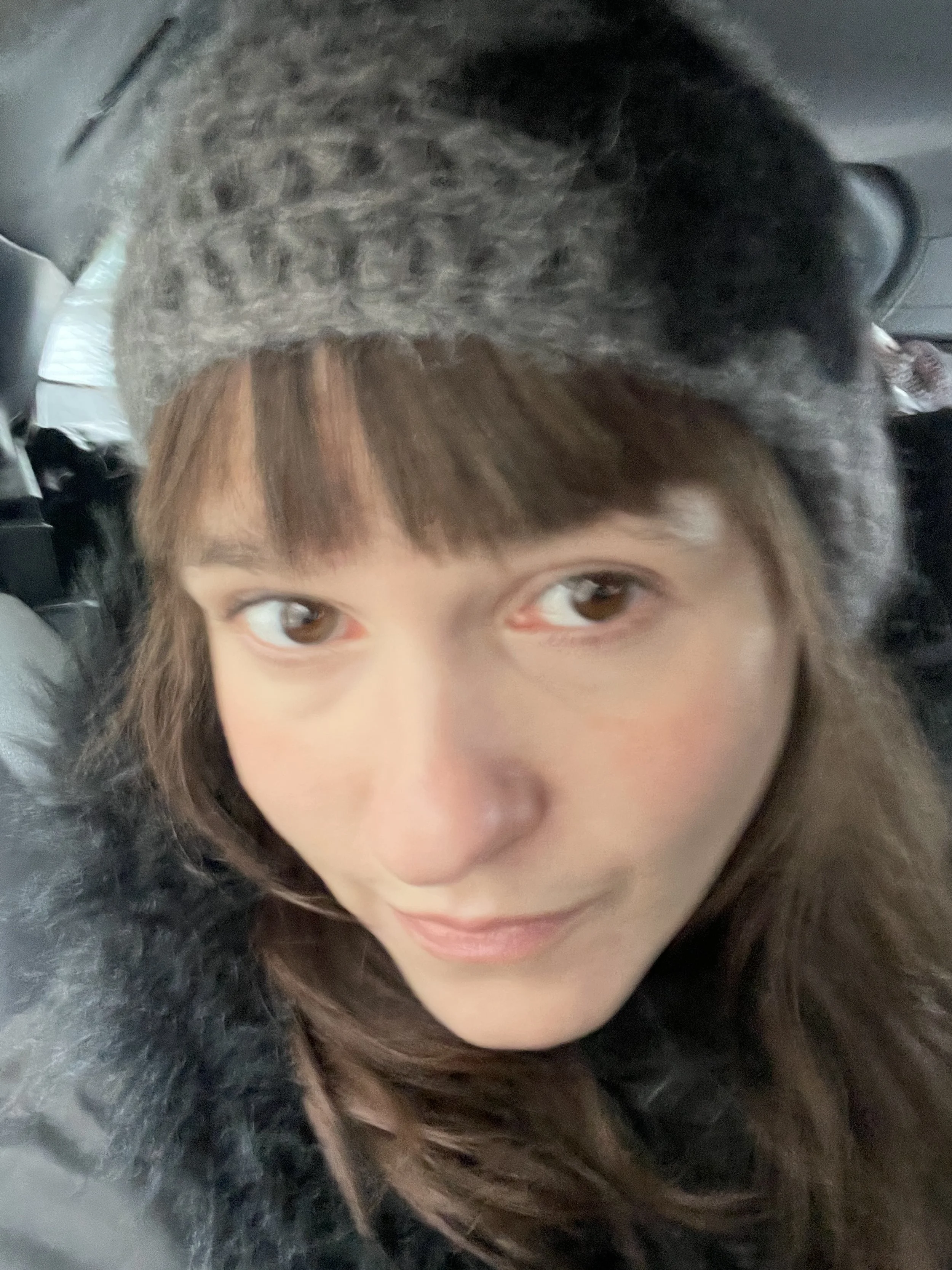Close-up of a woman wearing a gray knitted hat and a black coat, sitting in a vehicle.