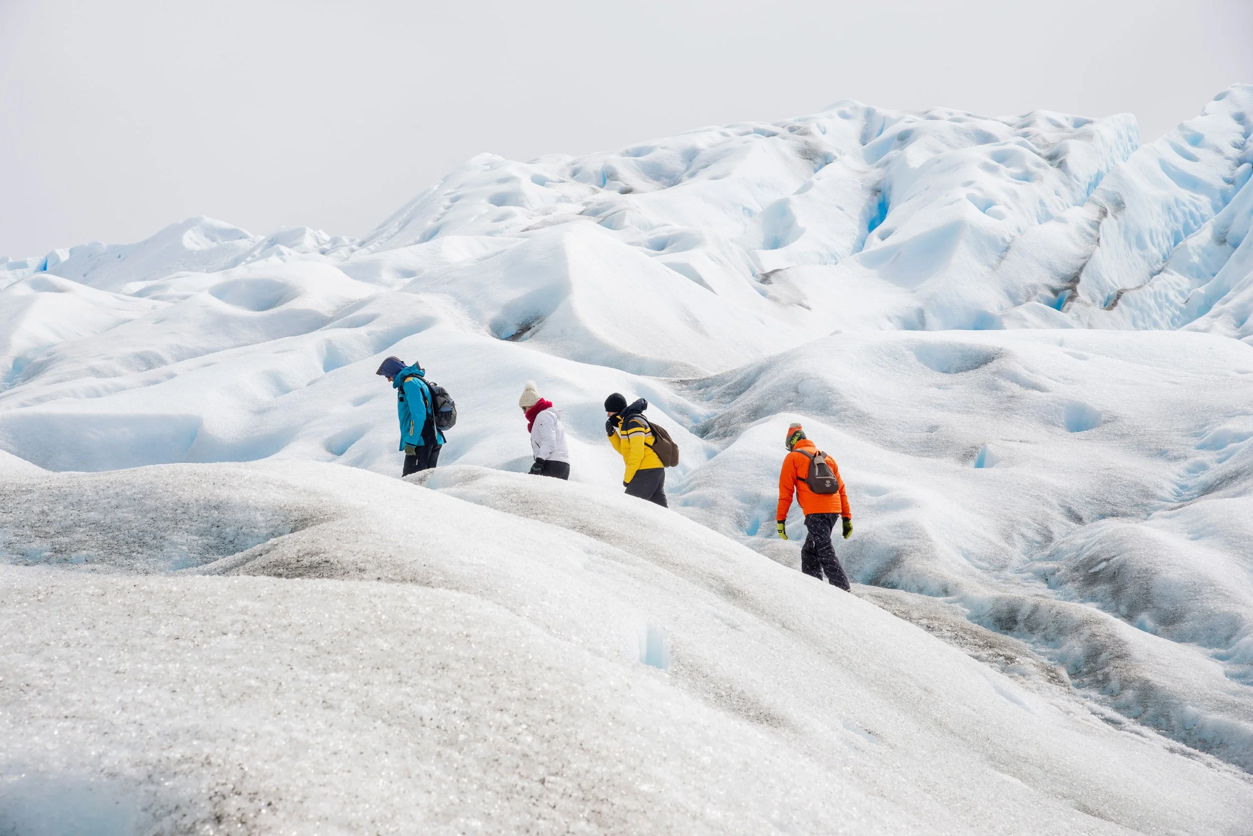 Grupo de personas caminando por un hielo glacial en un paisaje de nieve con niebla.