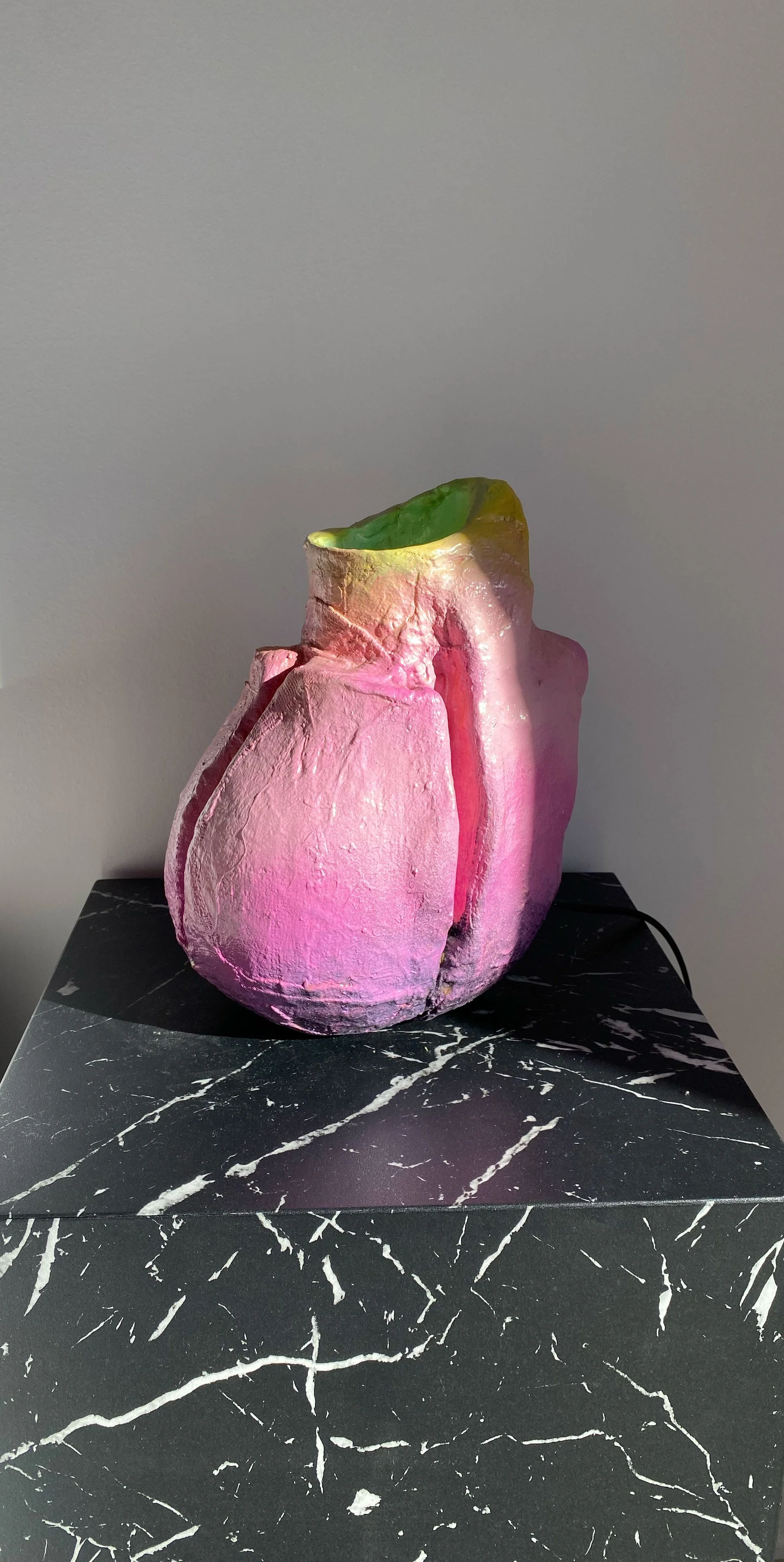 A pink and green ceramic vase placed on a black marble table.