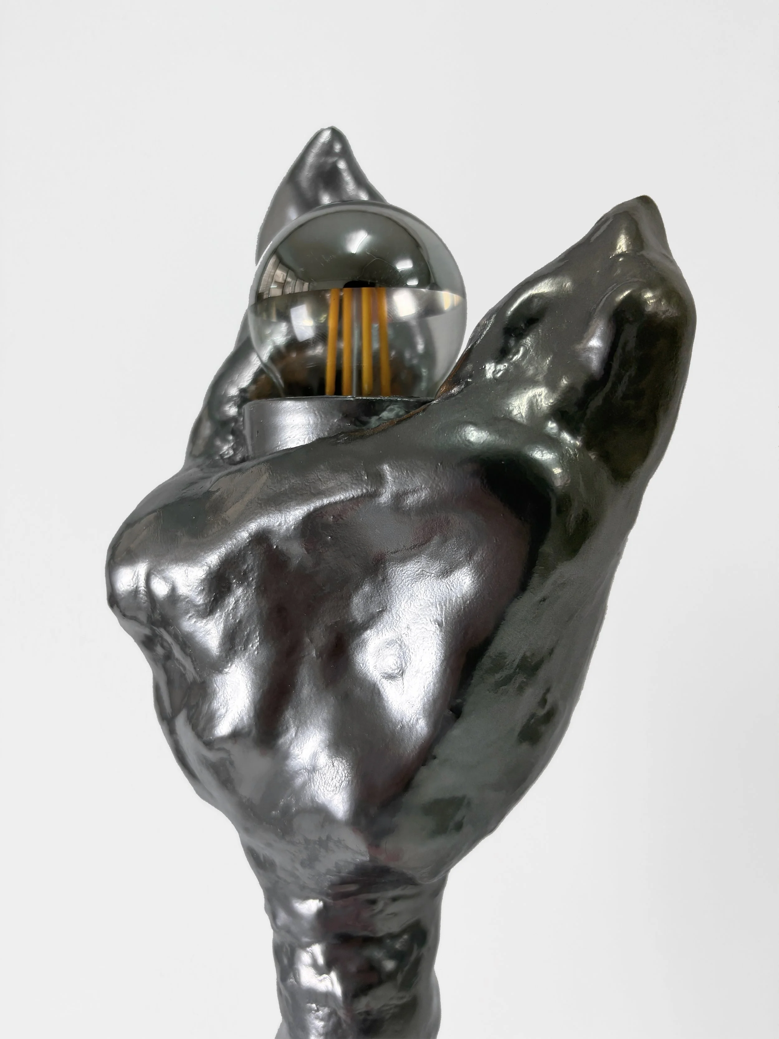 Abstract sculpture of a hand holding a reflective metallic sphere and a smaller sphere with a shiny, textured surface, set against a white background.