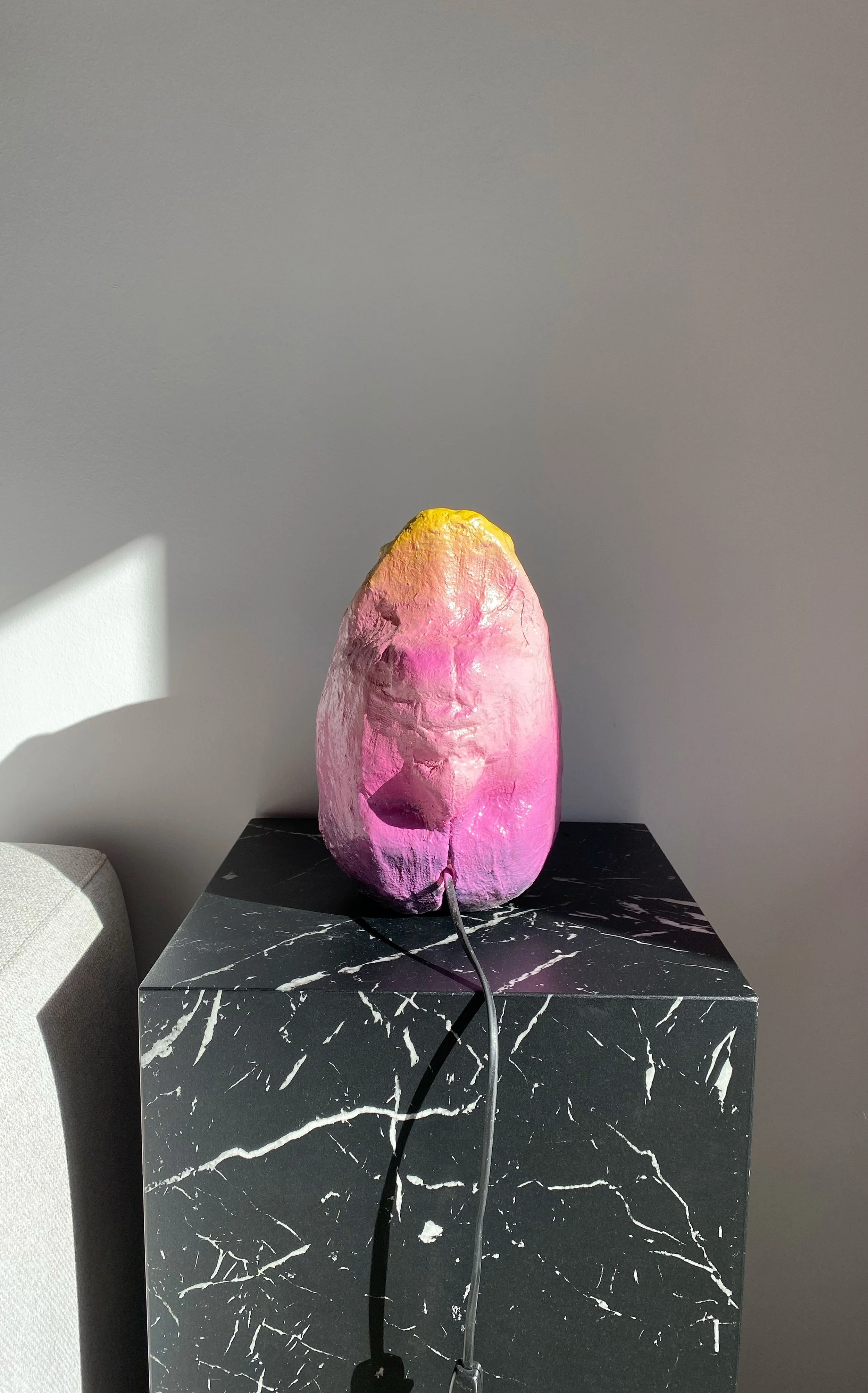 Pink and yellow textured sculpture on a black marble table, with a gray wall background.