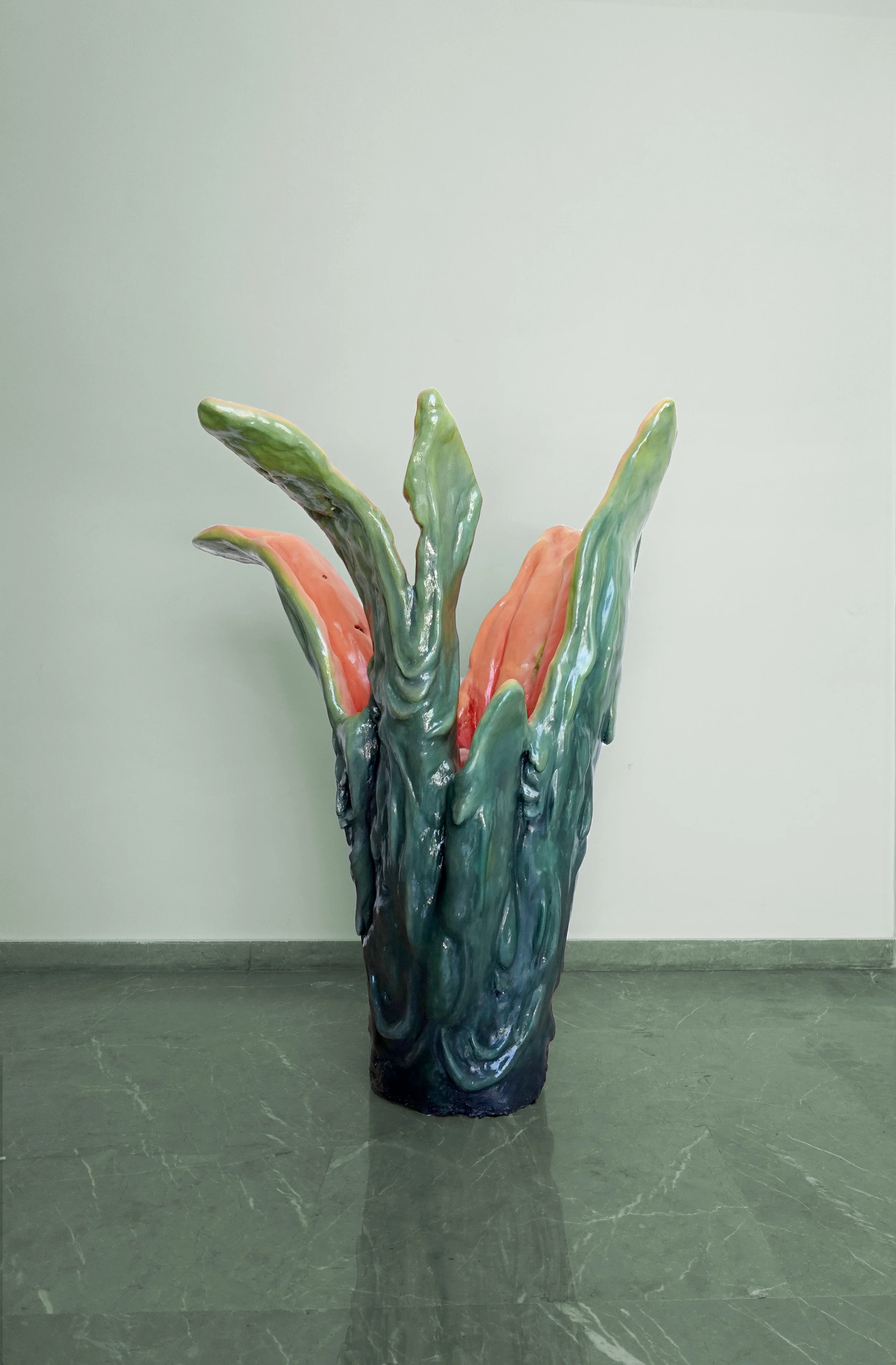 Colorful ceramic sculpture resembling a cactus plant with green and pinkish-orange parts, placed indoors against a light-colored wall.