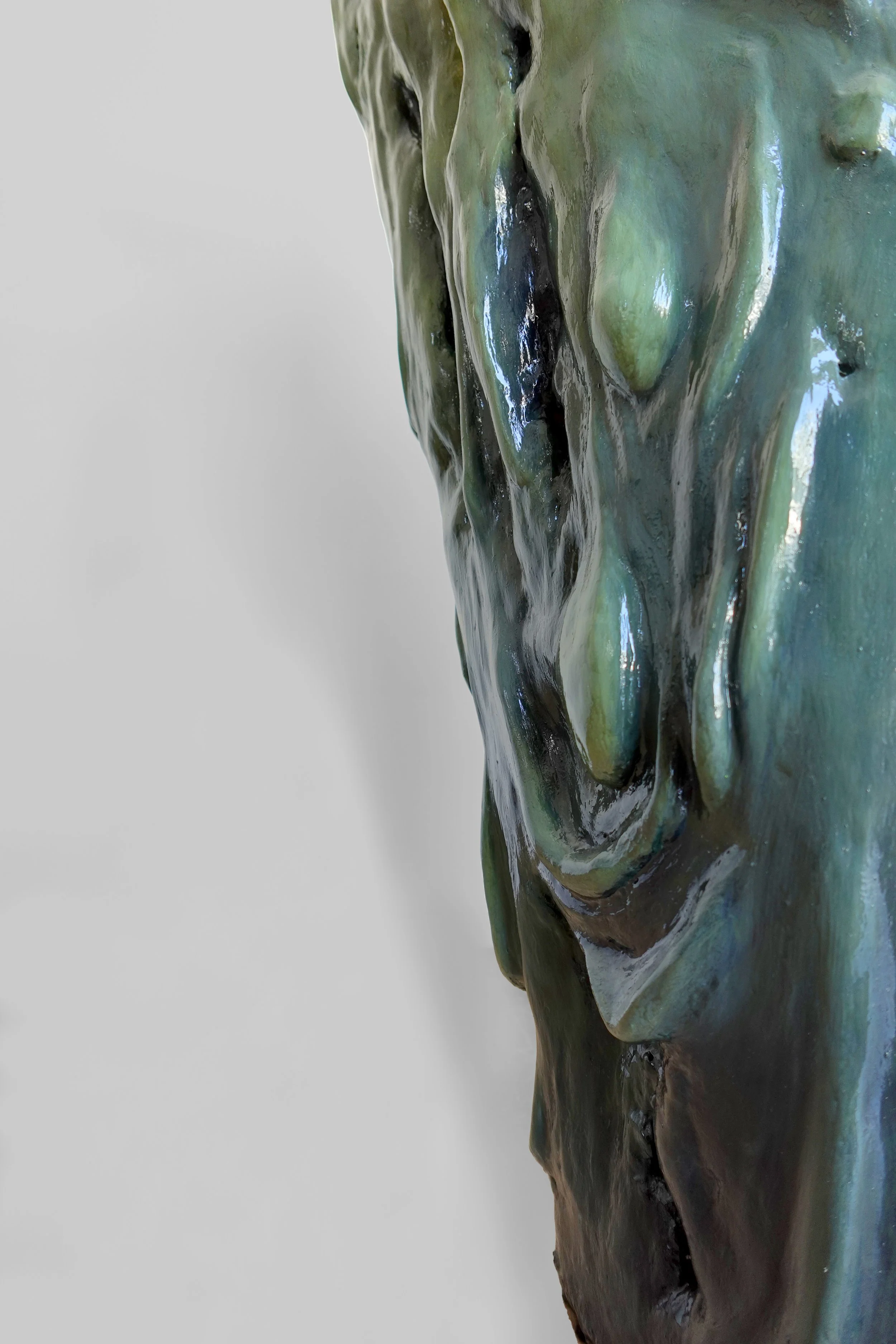 Close-up of a textured, glossy ceramic sculpture with abstract green, black, and brown hues.