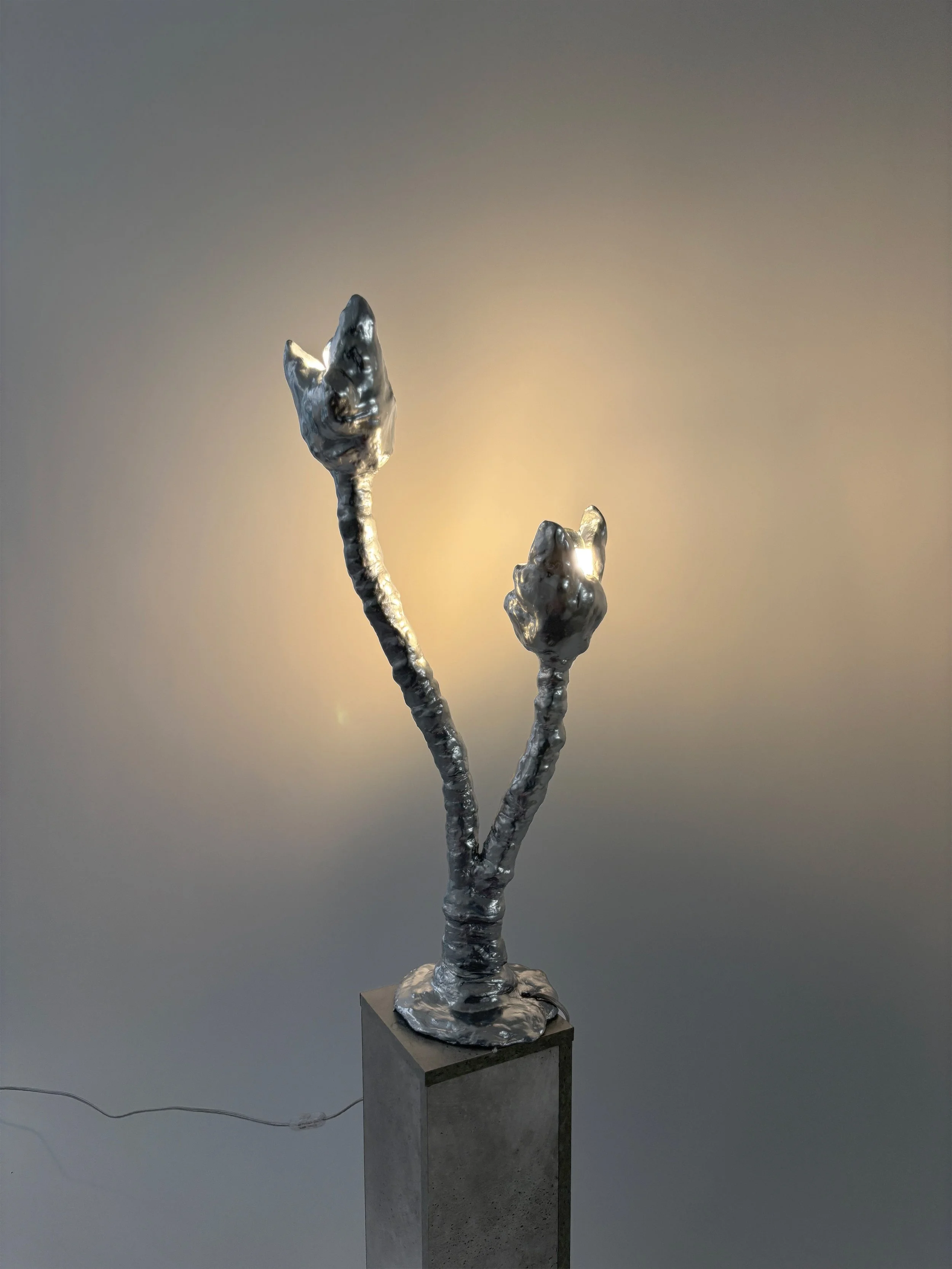 Bell-shaped metallic sculpture on a pedestal with a plain background