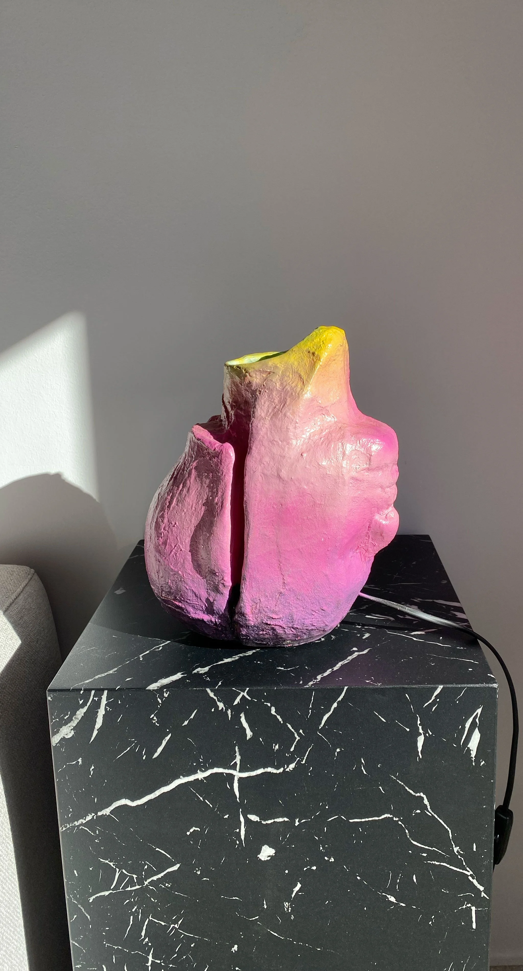 Colorful ceramic sculpture with pink and yellow hues on a black marble-patterned pedestal.
