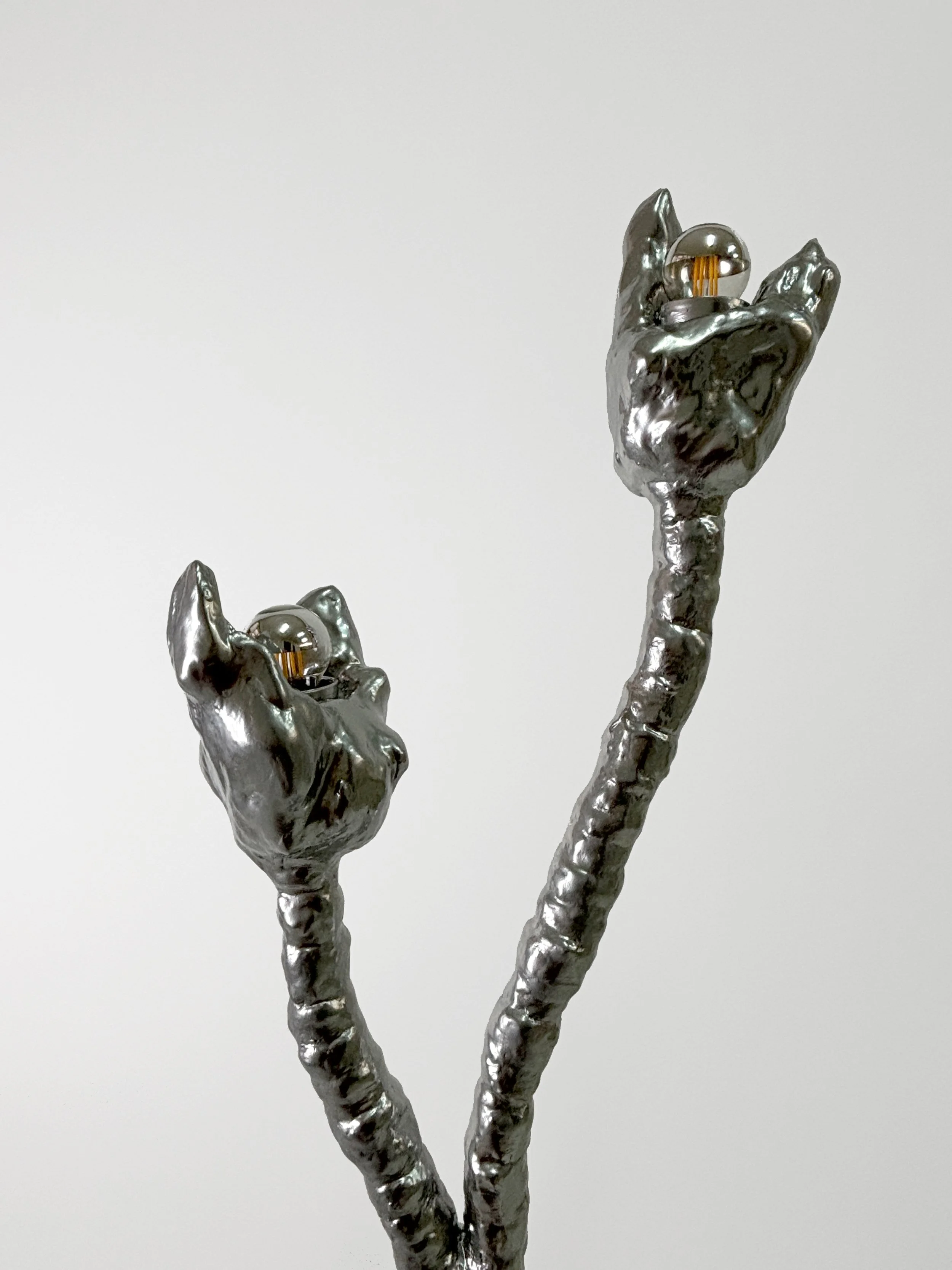 Metallic sculpture of two raised hands with light bulbs at the fingertips against a plain white background.