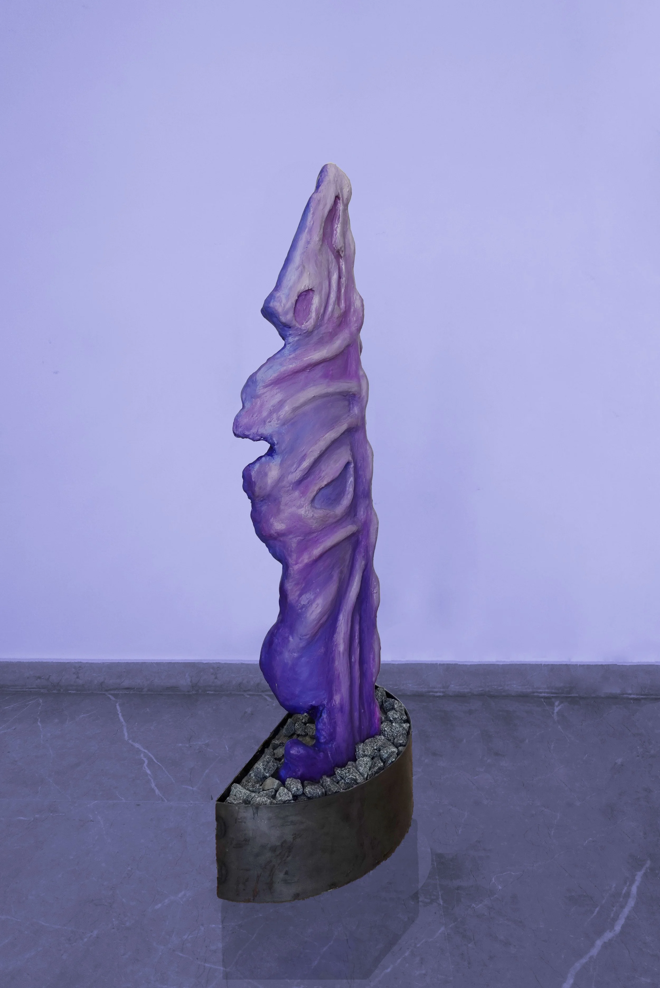 A purple abstract sculpture on a bed of rocks, set against a purple wall.