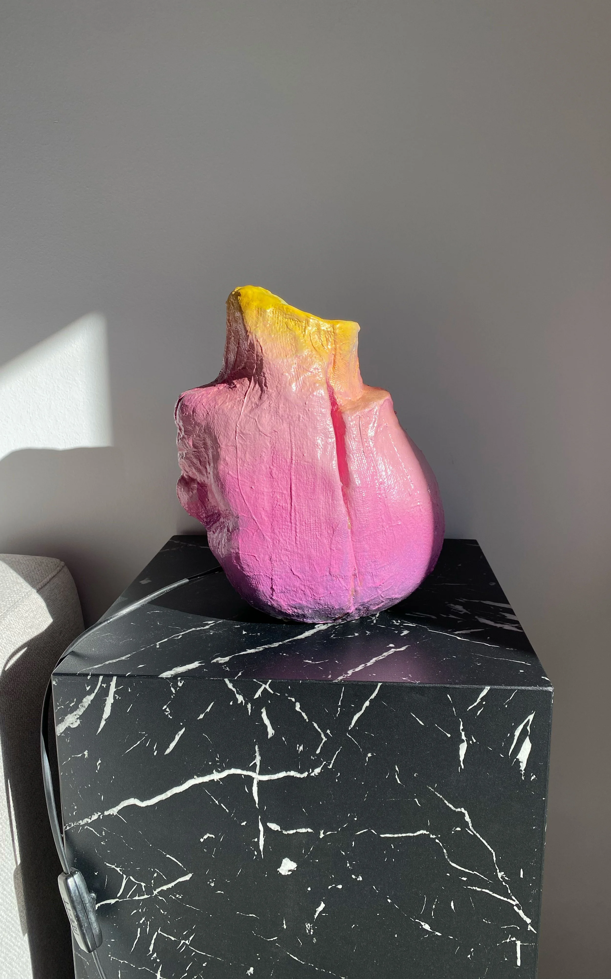 Colorful abstract sculpture on a black marble pedestal in sunlight.
