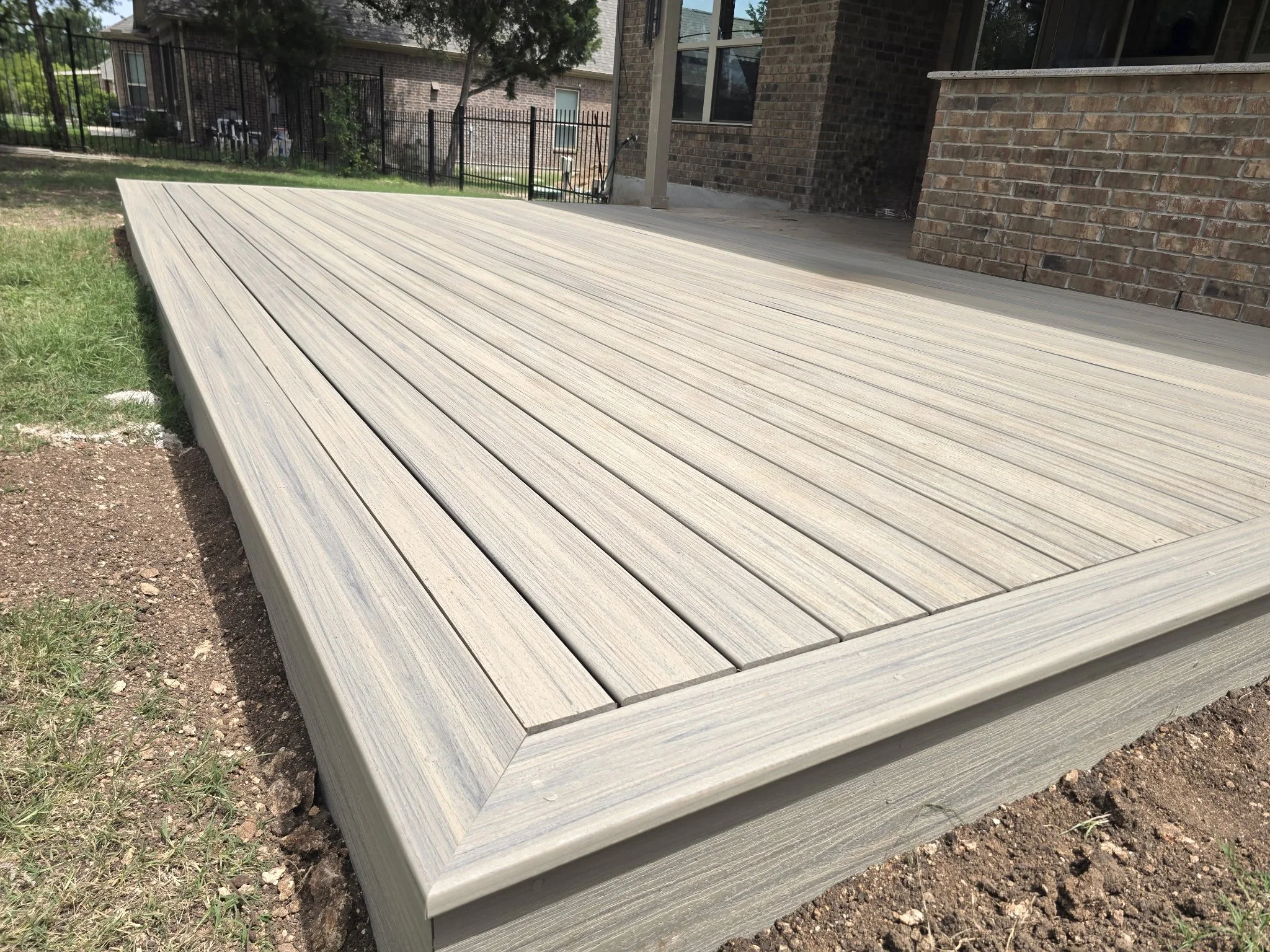 A wooden deck attached to a brick house with a grassy area and some gravel at the edge.