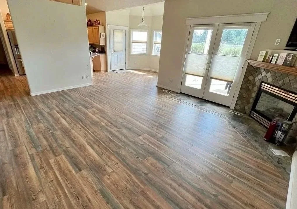 Empty living room with wood flooring, white walls, large glass doors, and a fireplace with a stone surround.