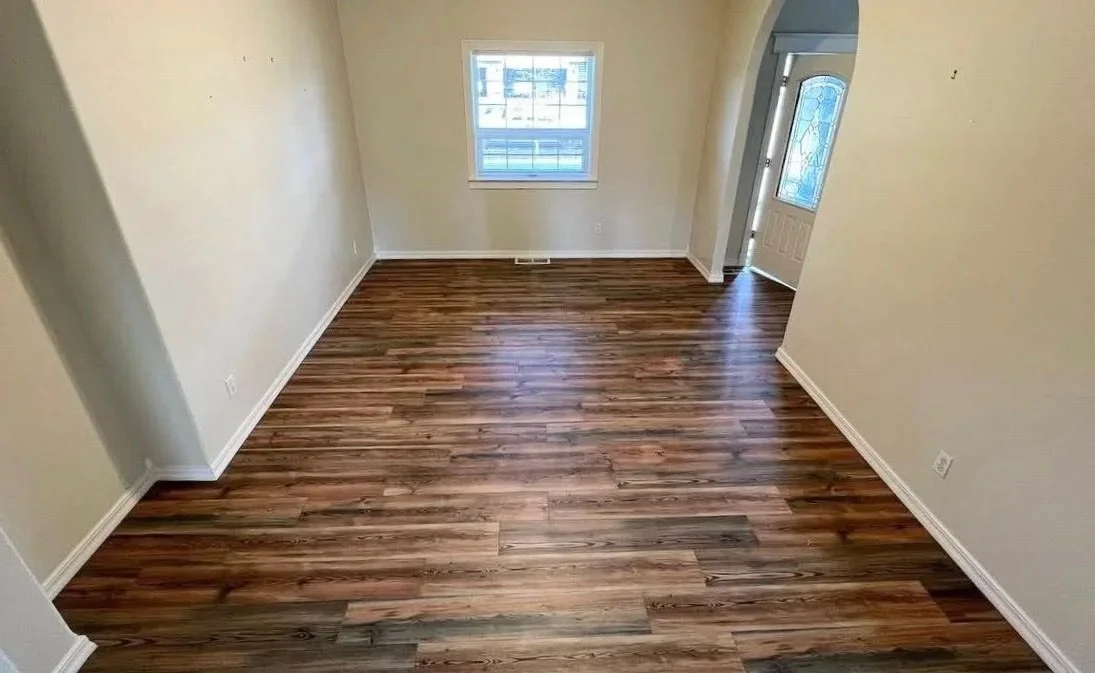 Empty room with hardwood floor, cream-colored walls, window, and door with glass window.