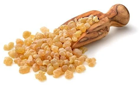 Frankincense resin granules with a wooden scoop on white background.