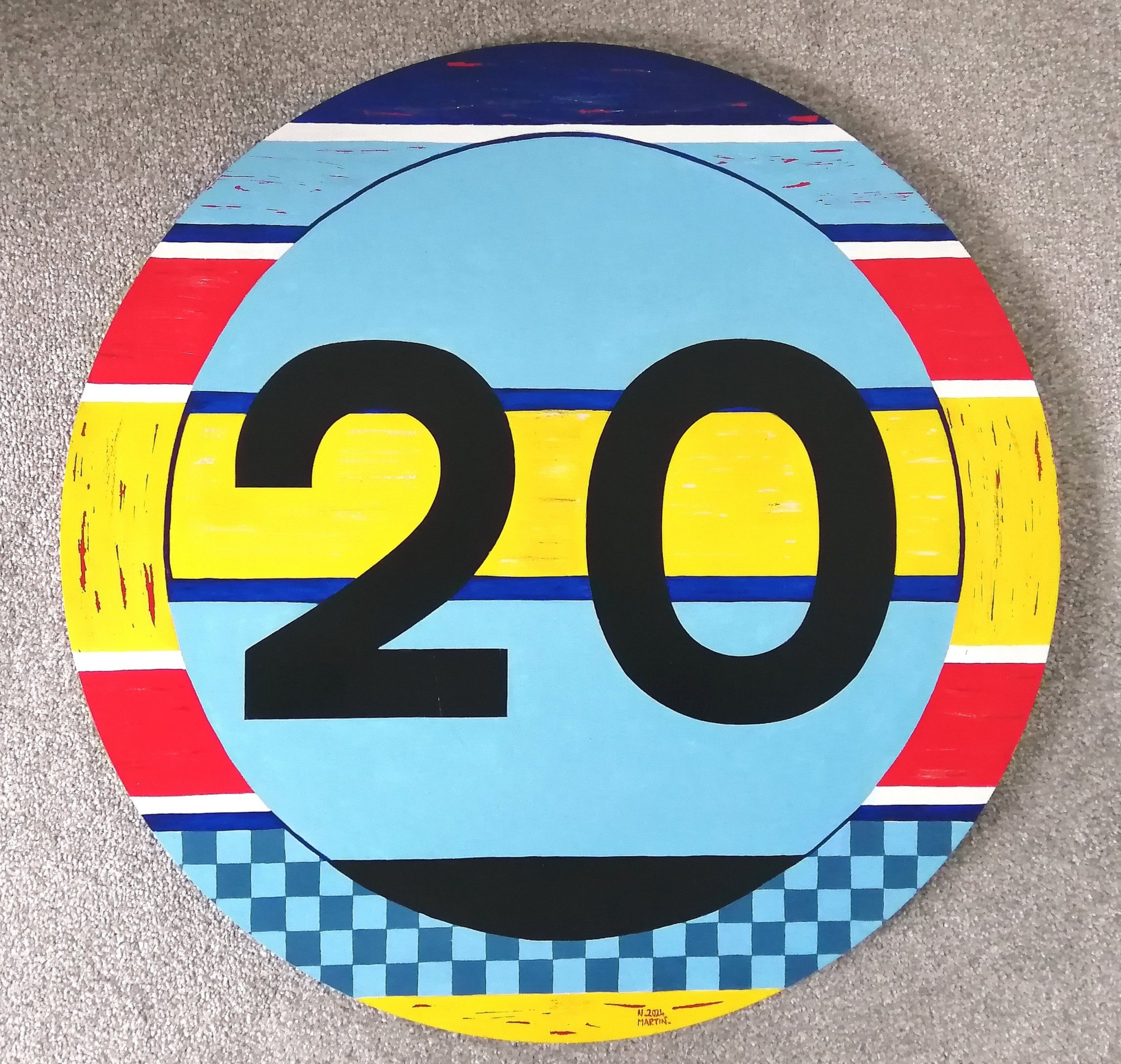 A round 20mph sign with a horizontal striped border in dark & light blue, white, red & yellow, with an inner circle with horizontal stripes in light & dark blue, yellow & black, with the 20 black