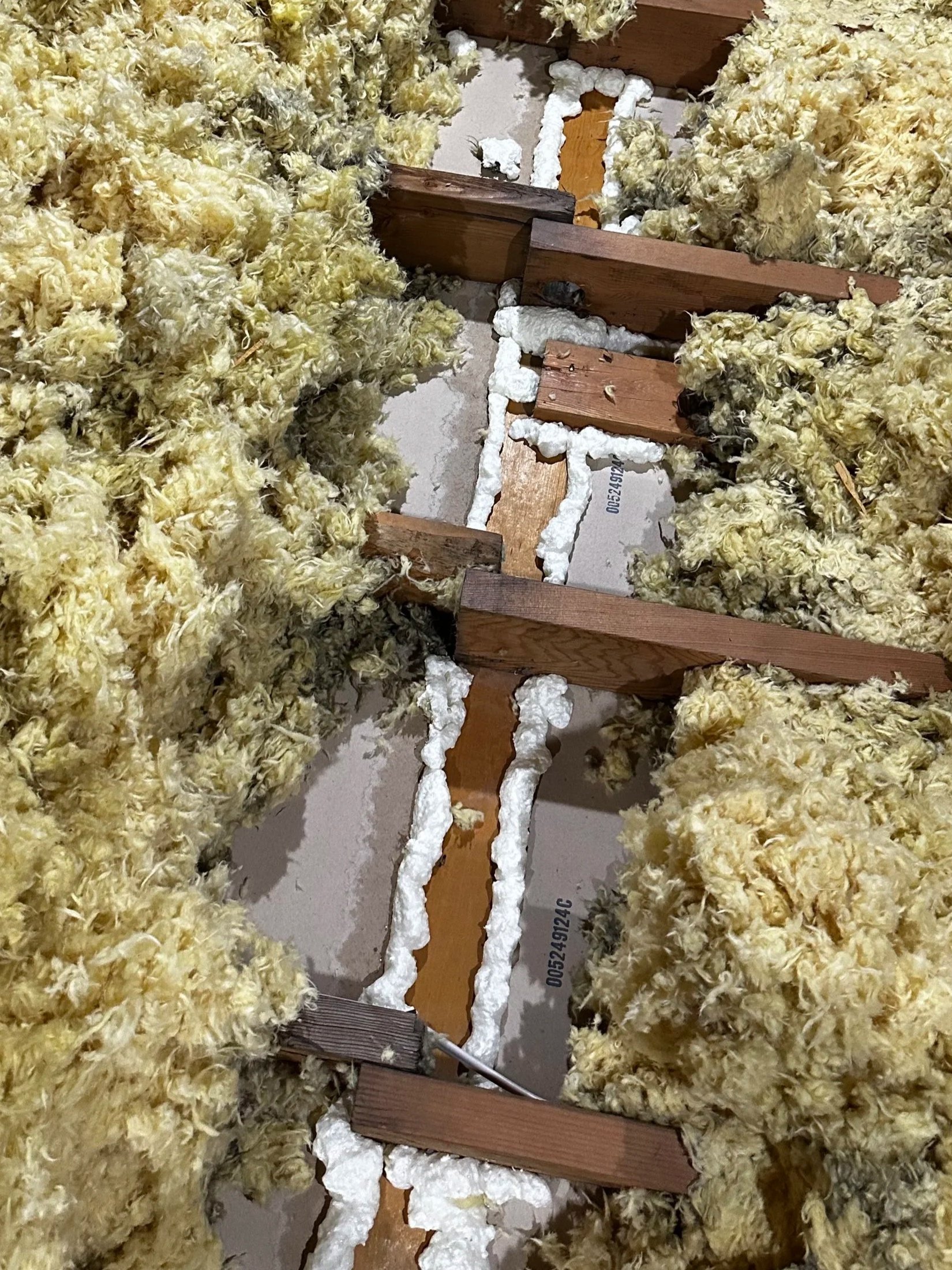Insulation and wooden framing in a wall under construction, with foam sealant applied around the edges.