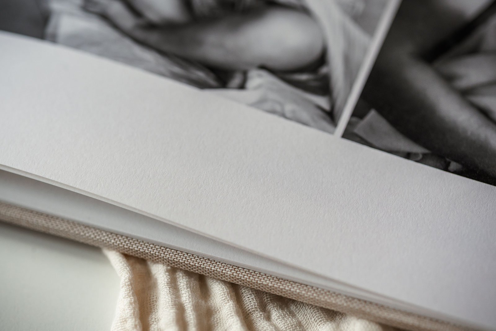 Nahaufnahme einer Seite eines geöffneten Buches mit schwarz-weißen Fotografien, liegend auf einem beigen Stoff.