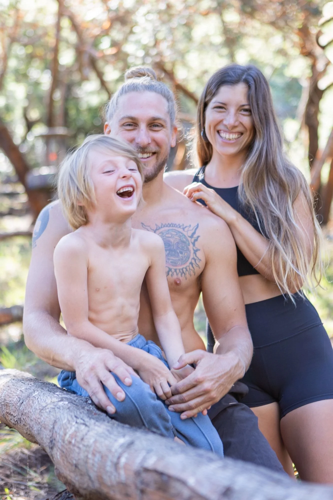 A family of three, a man, woman, and young boy, outdoors in a wooded area, smiling and enjoying time together on a sunny day.