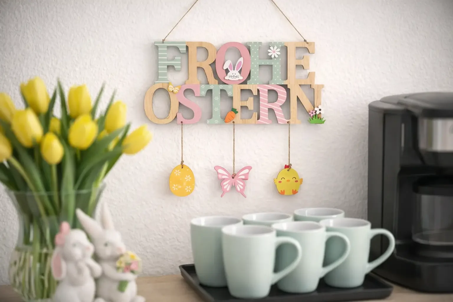 Kaffee-Ecke mit Frohe-Ostern-Schild, gelben Tulpen, pastellgrünen Tassen und schwarzer Kaffeemaschine