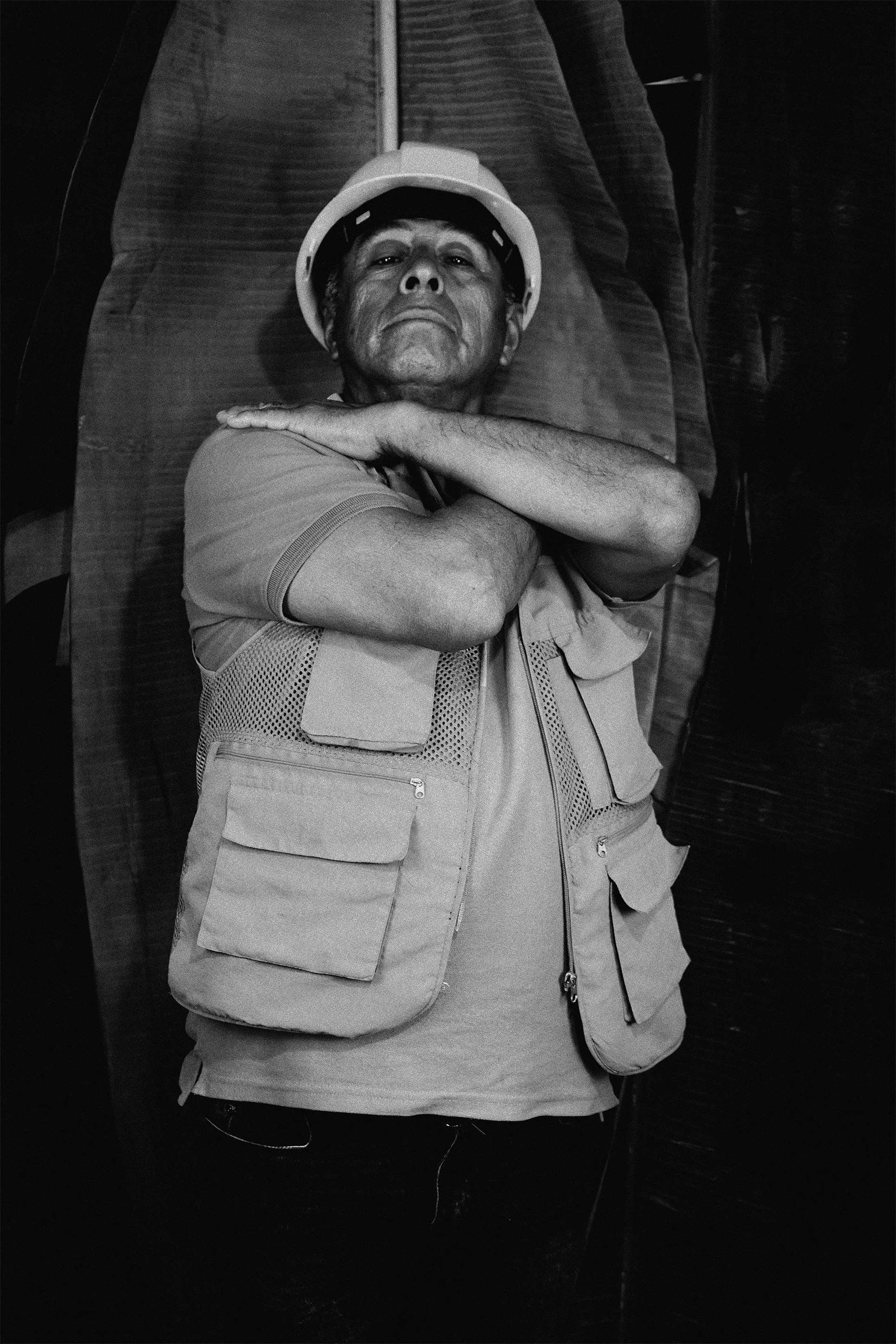 Hombre con casco de construcción descansando en una silla, con brazos cruzados sobre el pecho, en una fotografía en blanco y negro.