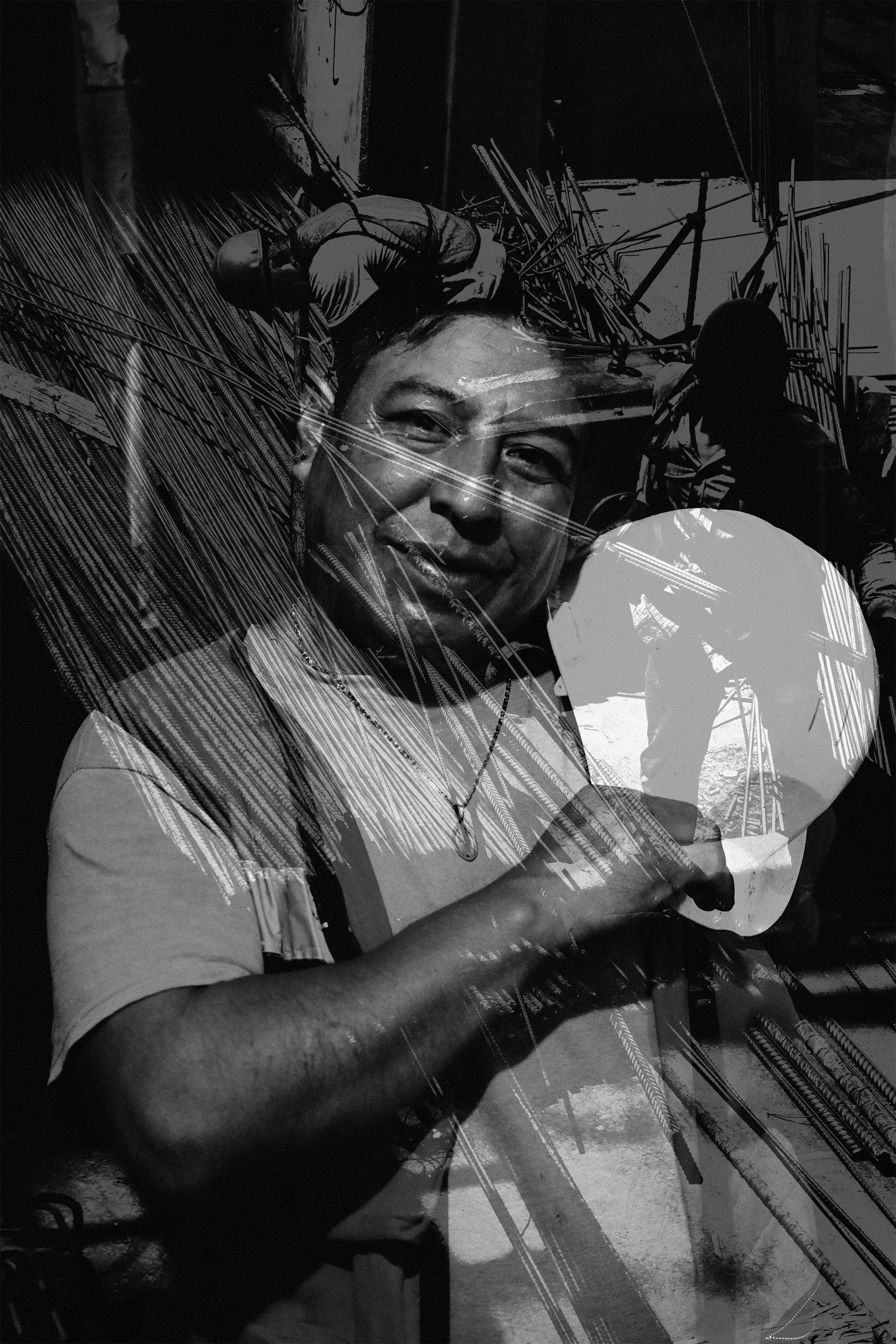 Hombre sonriendo con un martillo en mano, trabajando en la construcción o soldadura, con otros trabajadores en el fondo, en un entorno industrial o de construcción.