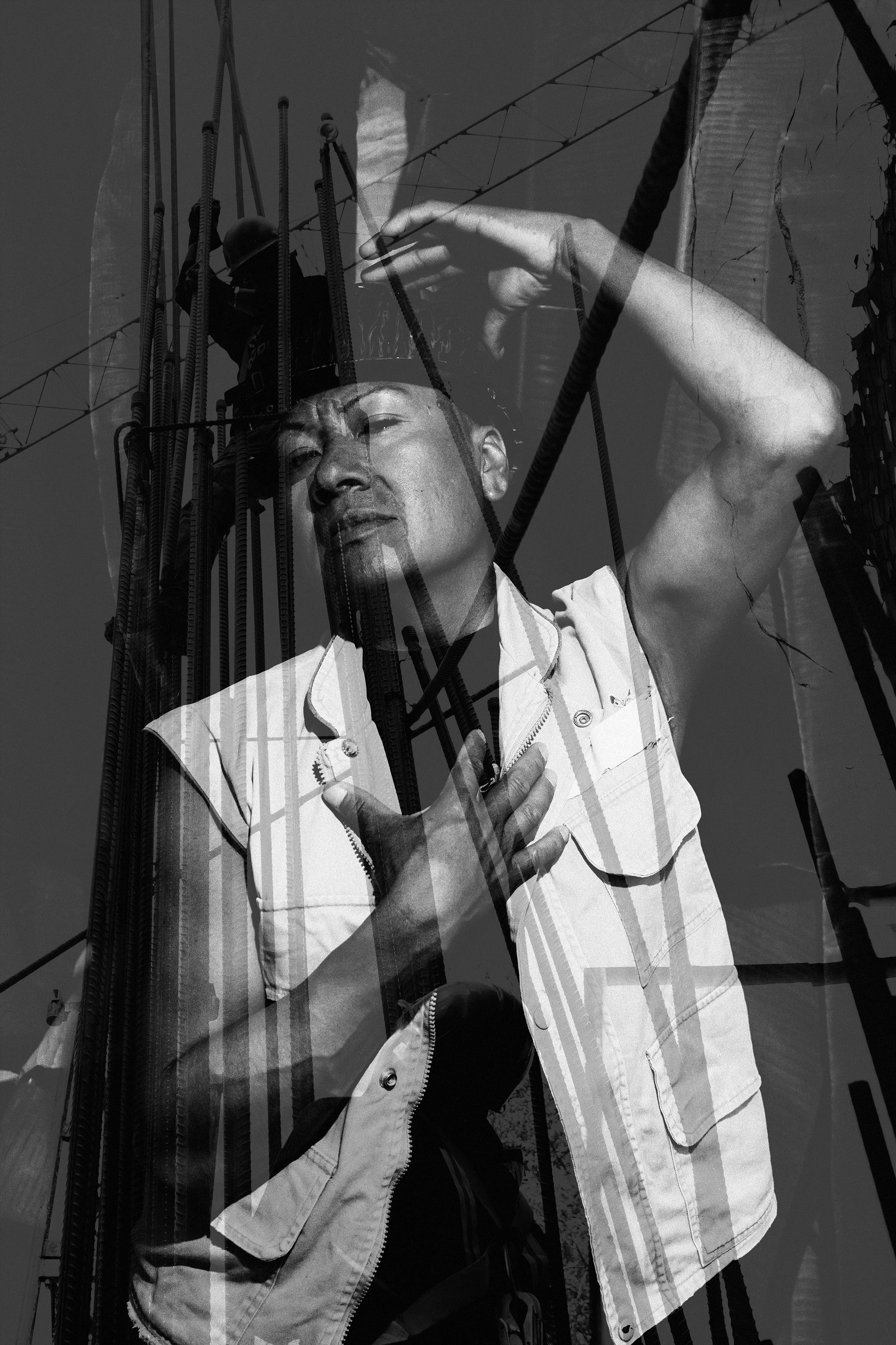 Una persona con una mano en el pecho, en una superposición con una estructura de construcción y un cielo despejado, en una imagen en blanco y negro.