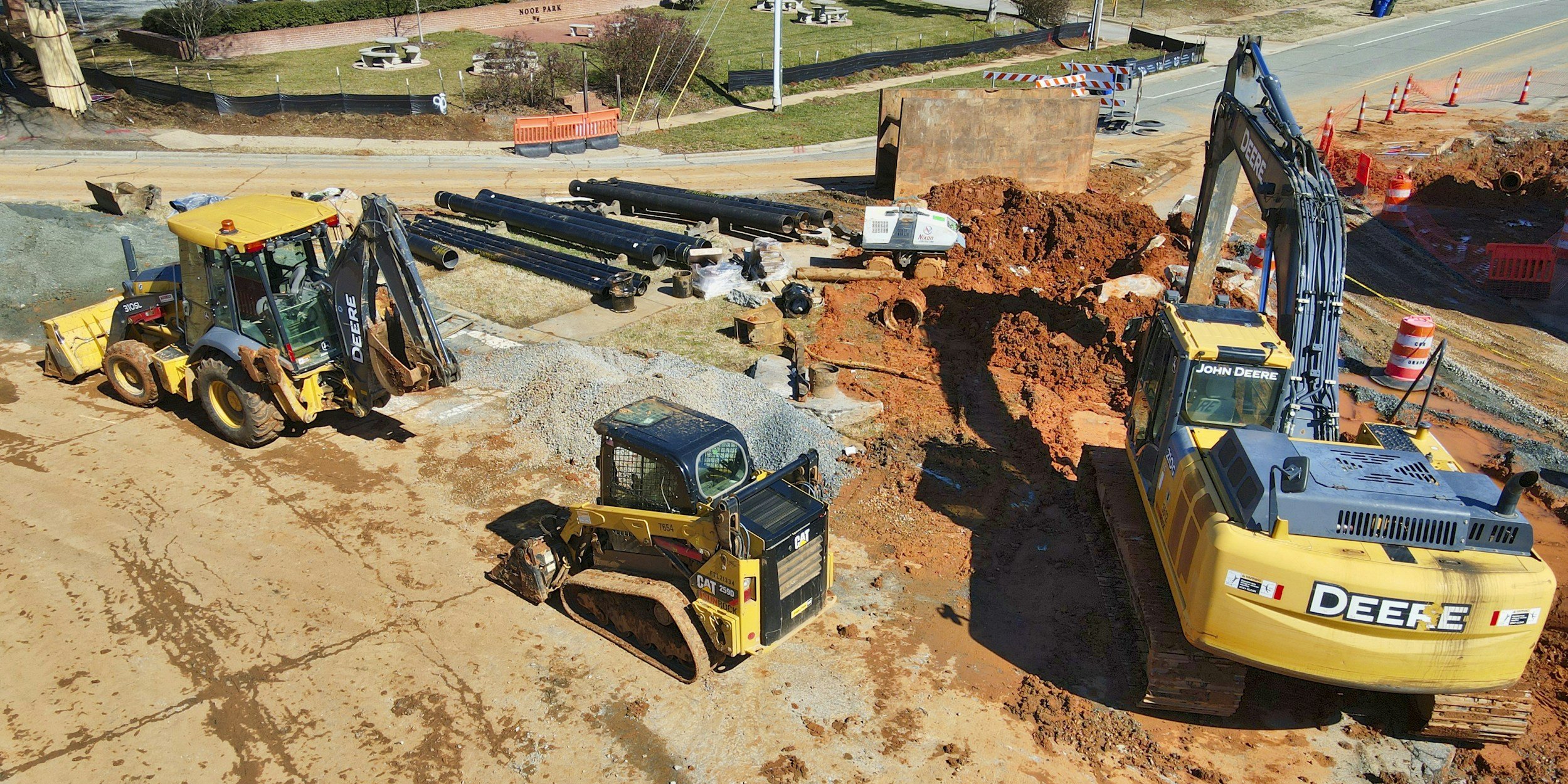 Construction site with excavators and bulldozers working on a road or building foundation, surrounded by dirt and construction materials.