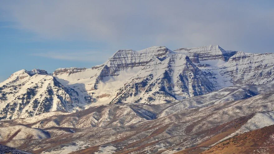 Snow-capped mountains under a cloudy sky with rocky and snowy terrain in the foreground.