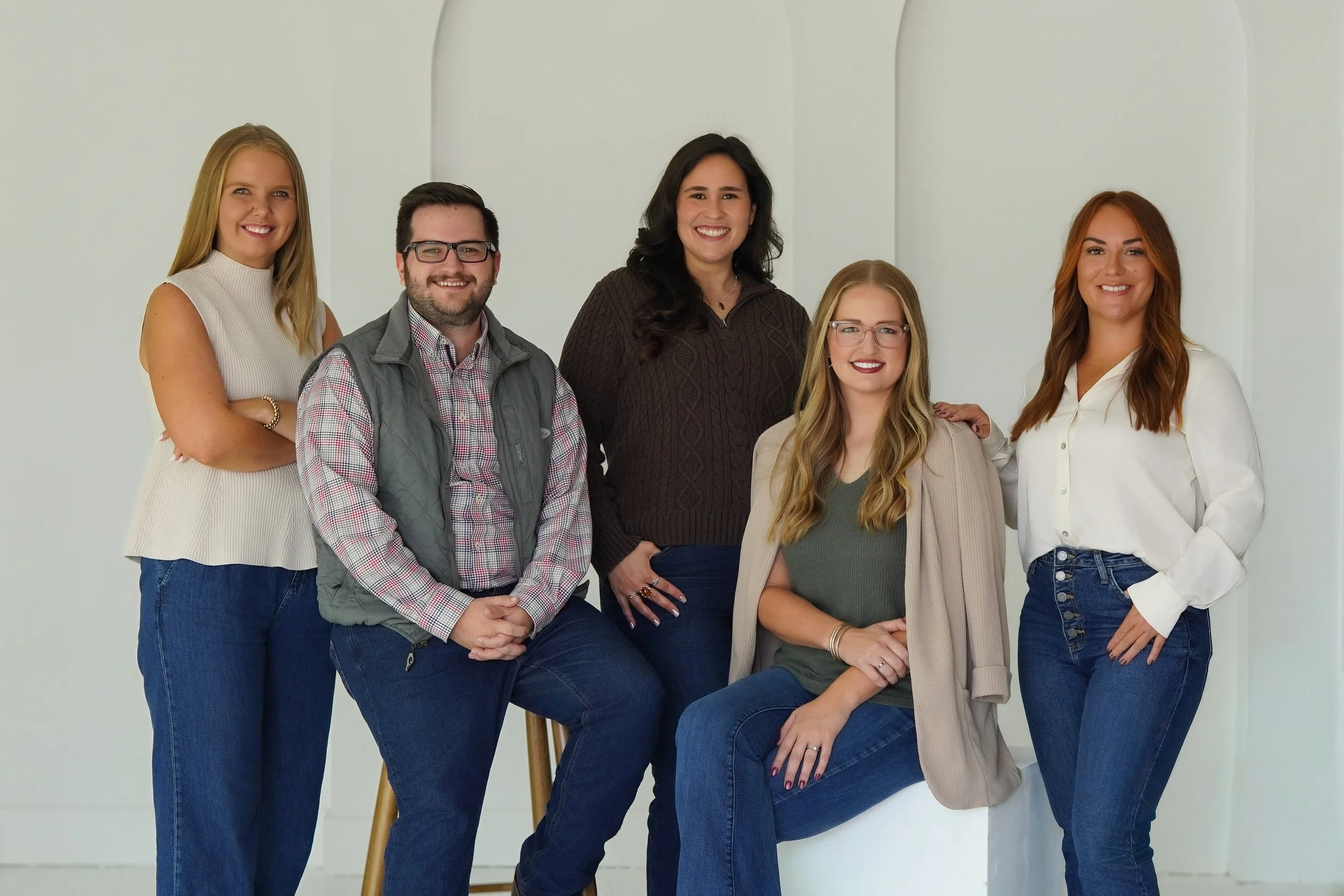 Group of six diverse young adults smiling and posing together against a plain white background.