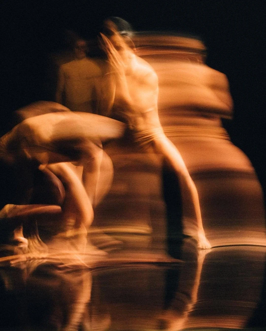 Imágenes borrosas de varias personas desnudas en movimiento en un fondo oscuro, con reflejos en una superficie.