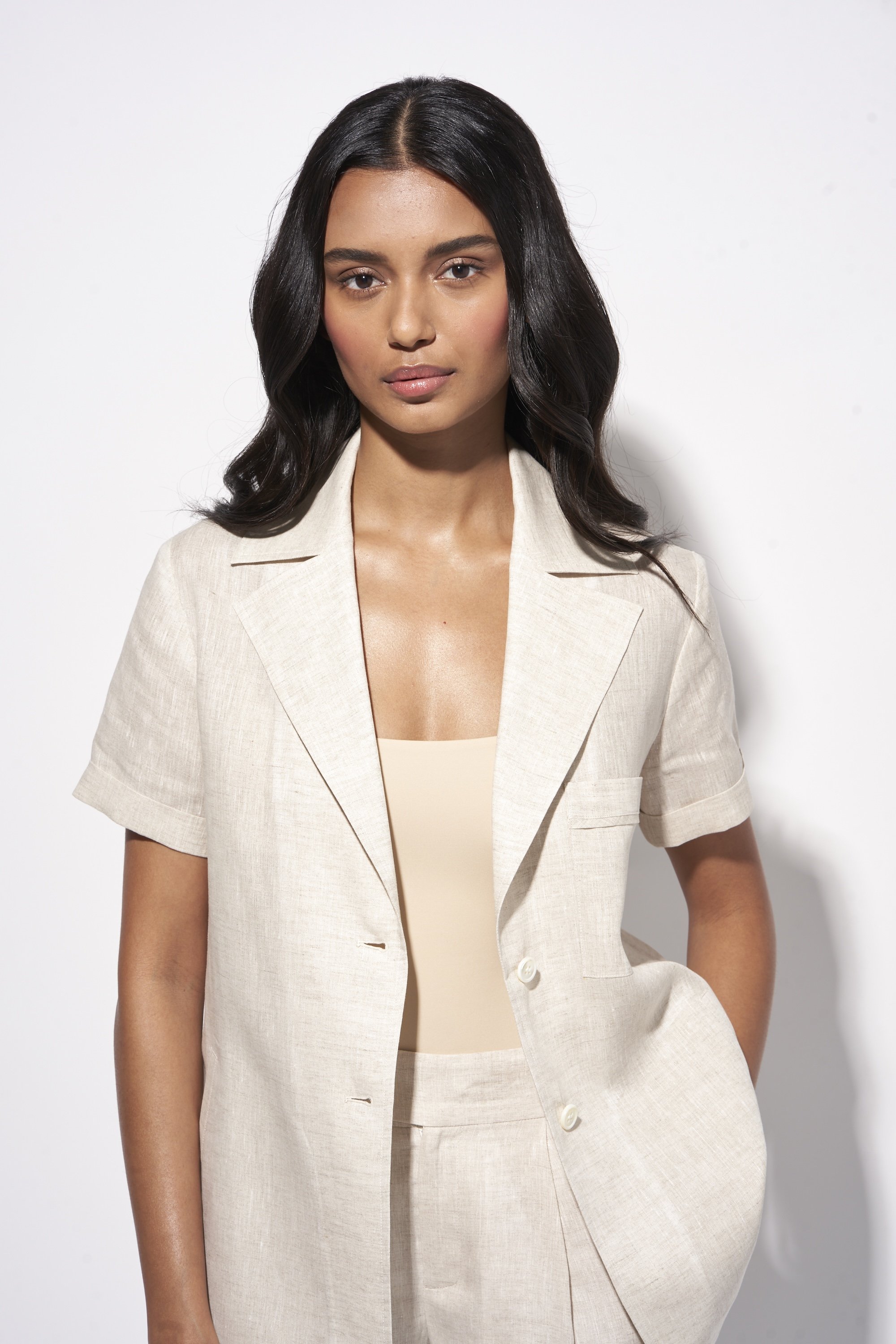 Person wearing a beige blazer and top against a white background