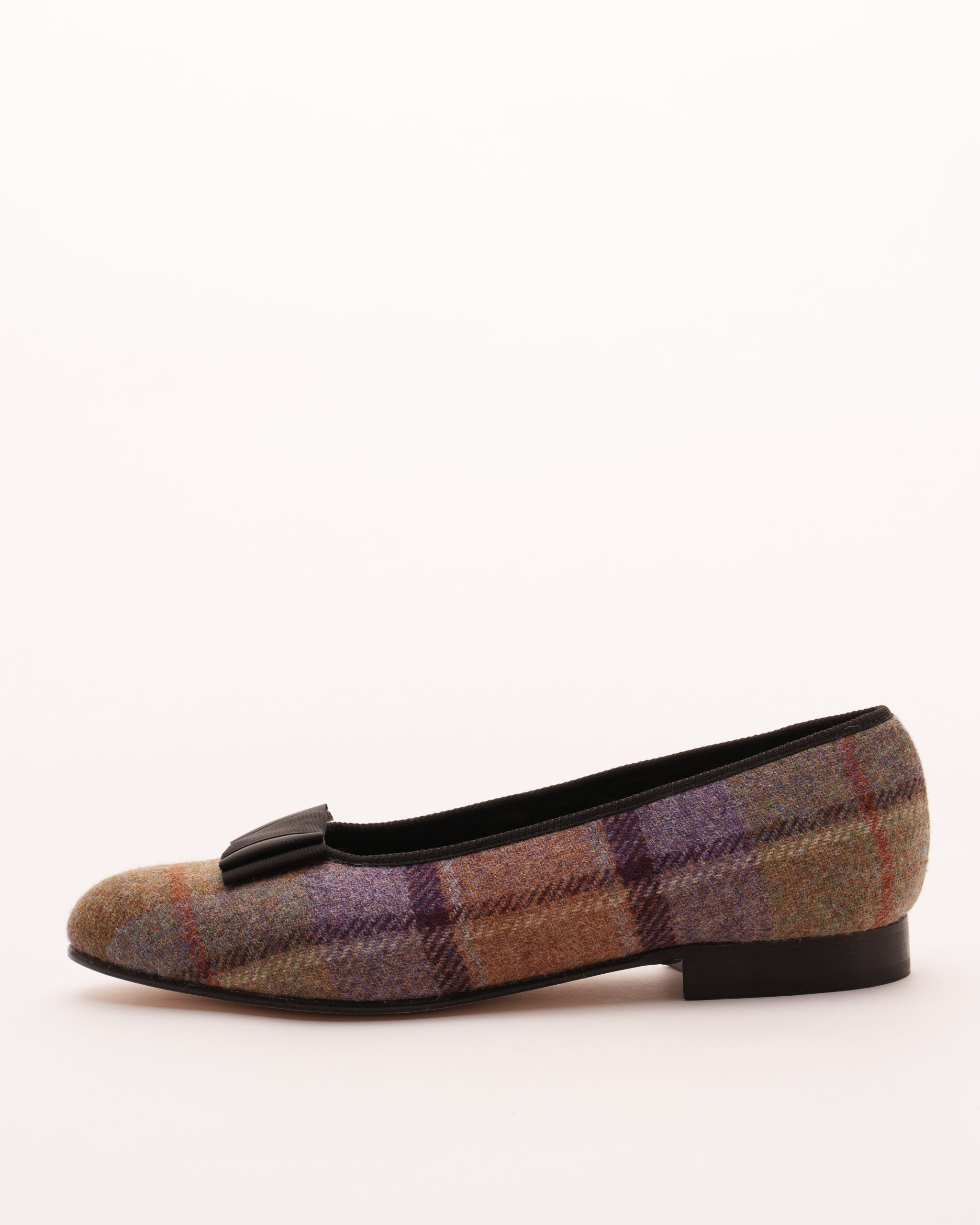 Plaid fabric flat shoe with black bow accent on a white background.